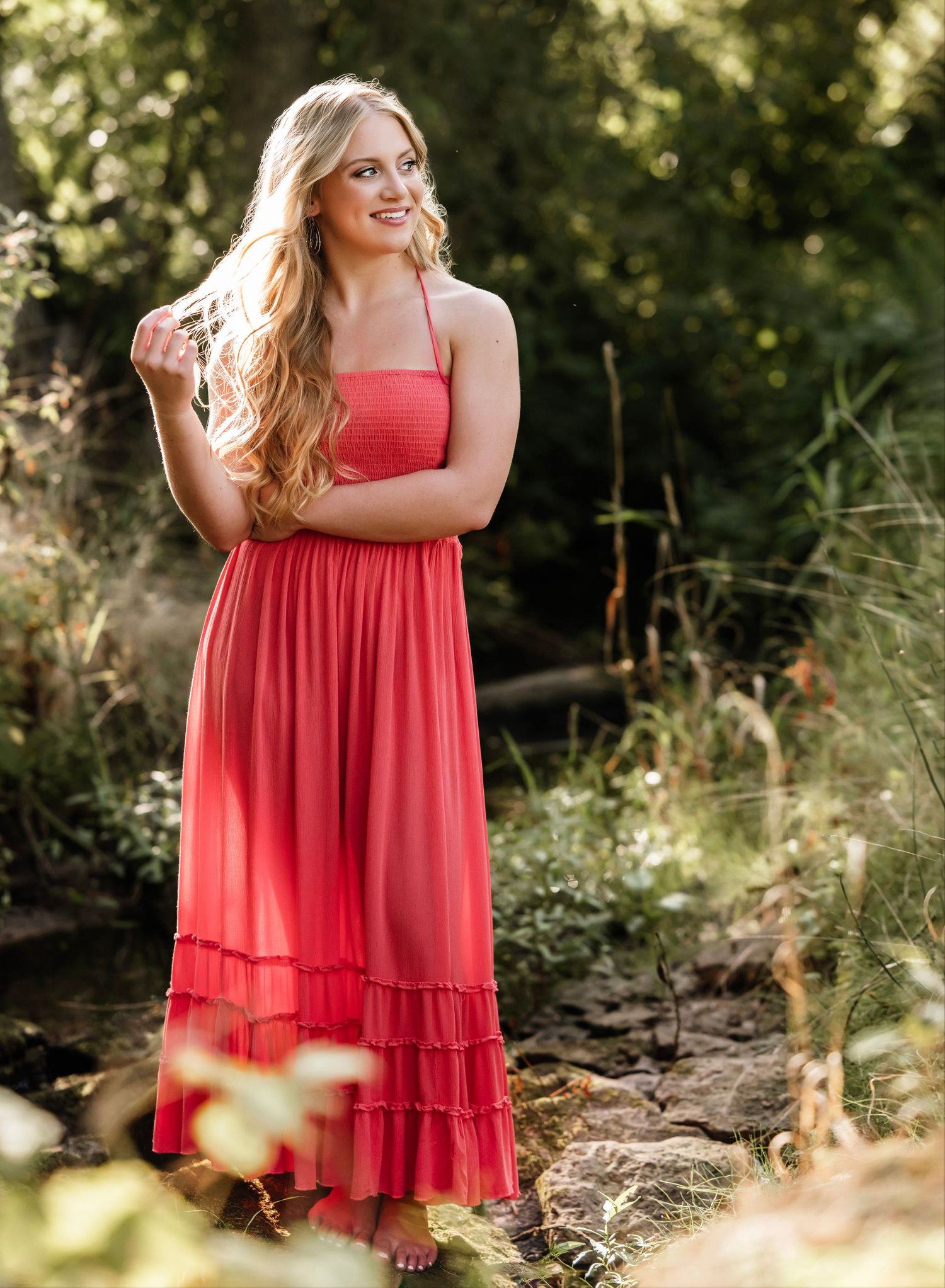 A flowing red tiered dress catches sunlight in a dreamy outdoor photoshoot among natural foliage.
