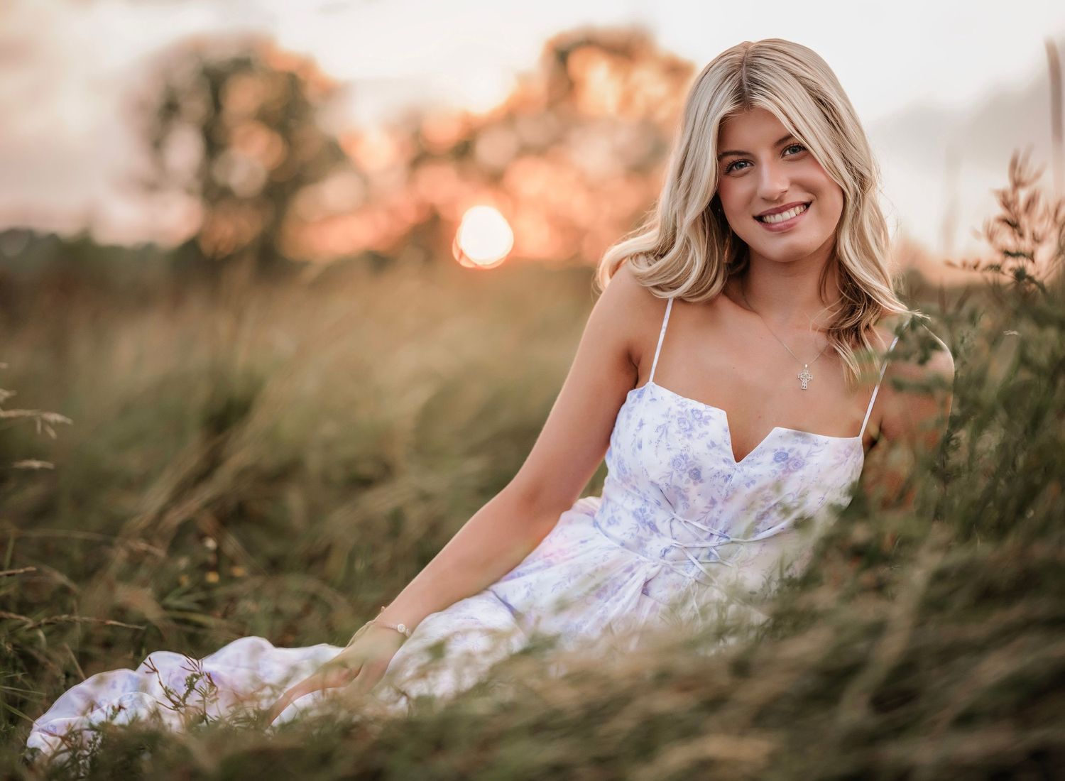 A bride in a white lace wedding dress poses in a grassy field during golden hour sunset.