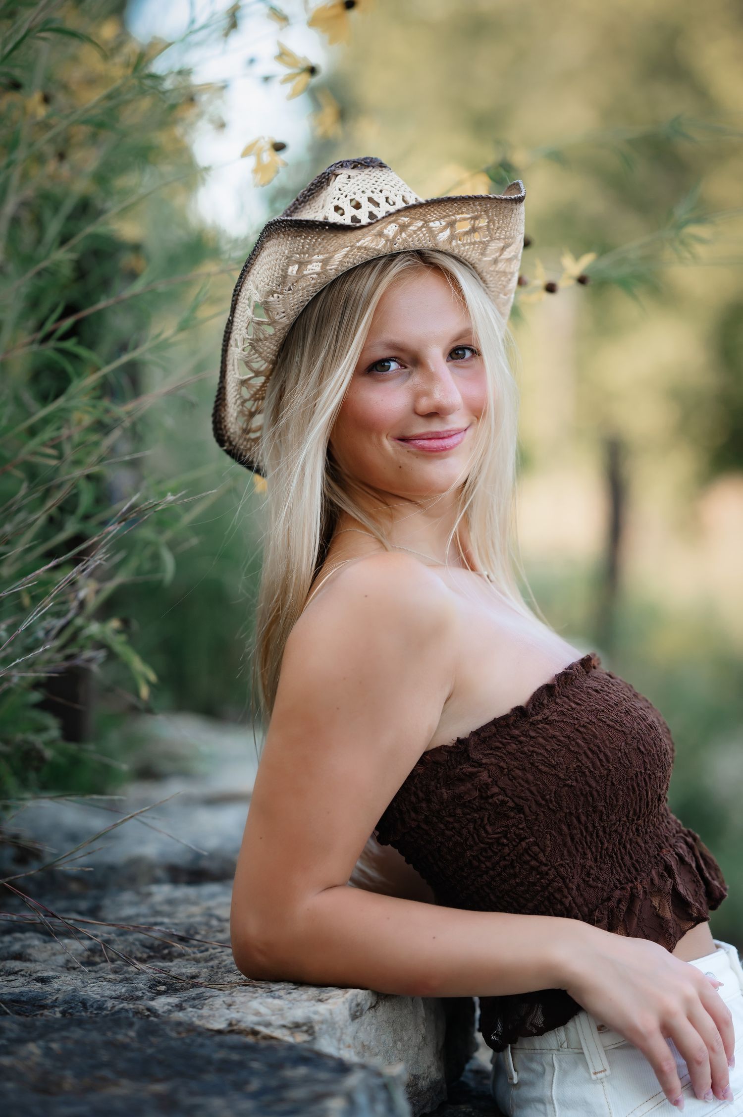 Countryside senior portrait featuring a brown dress and decorative straw hat in natural lighting.
