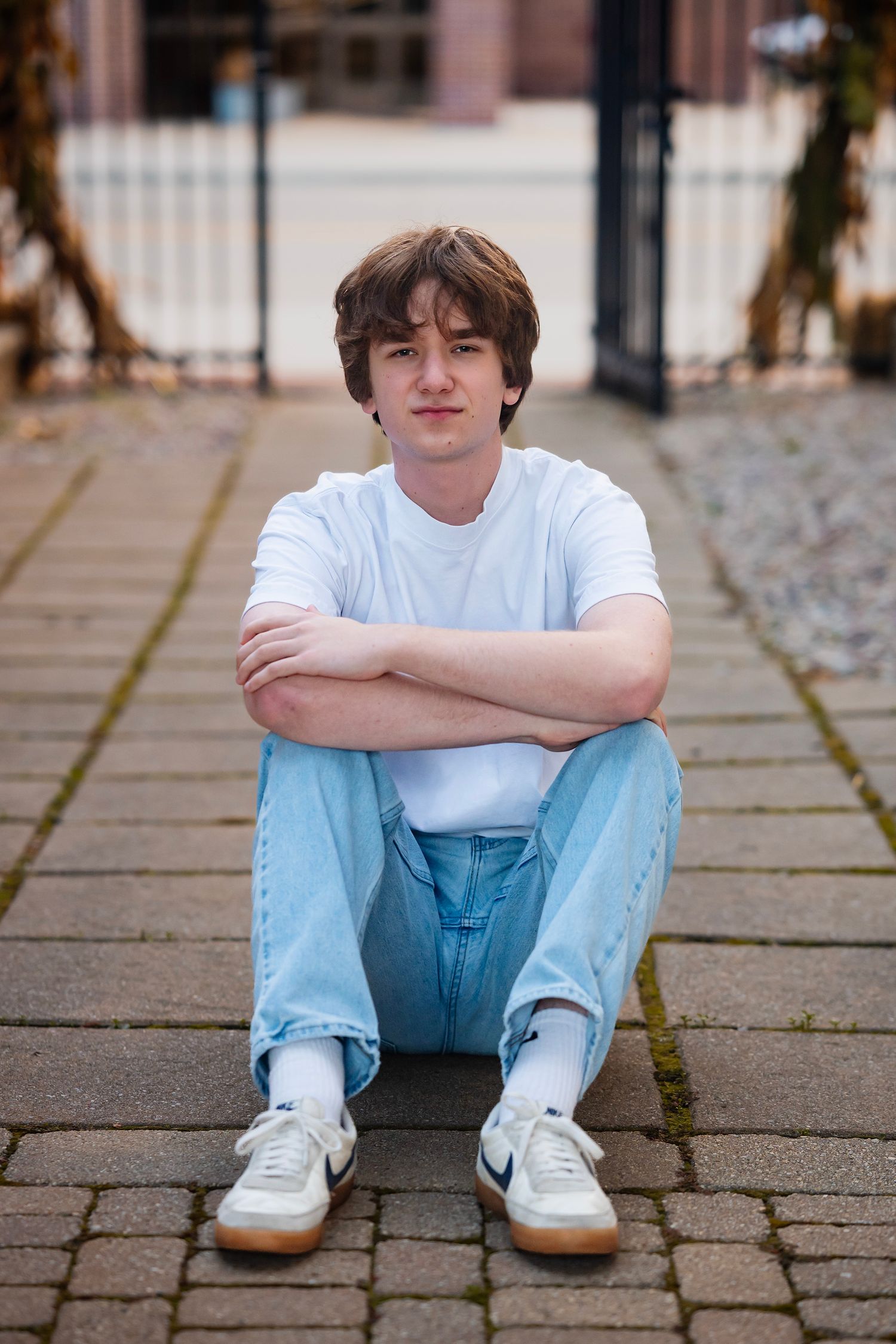 Person in white t-shirt and light blue jeans sitting on stone pavement in urban setting.