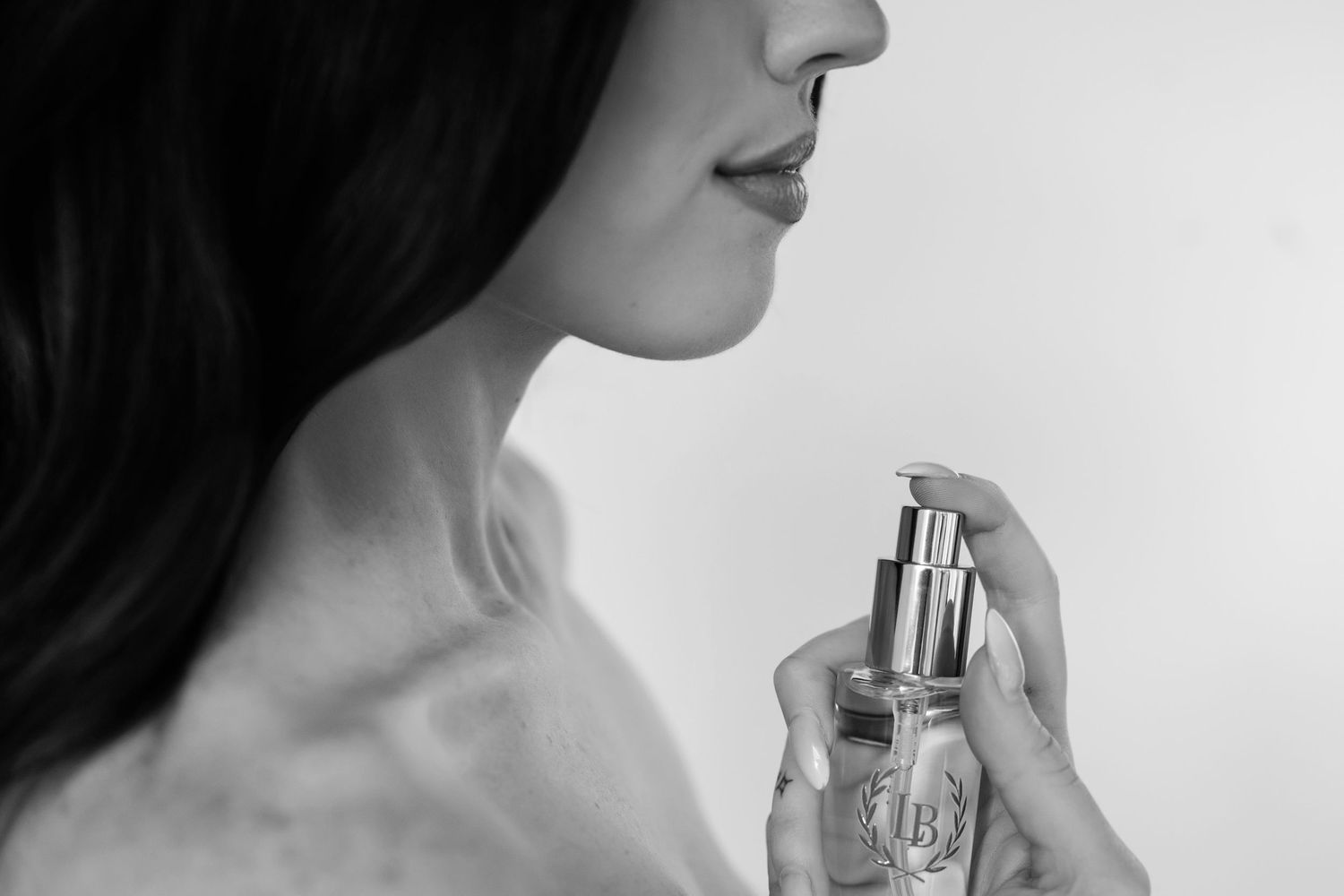 Black and white close-up photo of someone applying perfume to their neck.