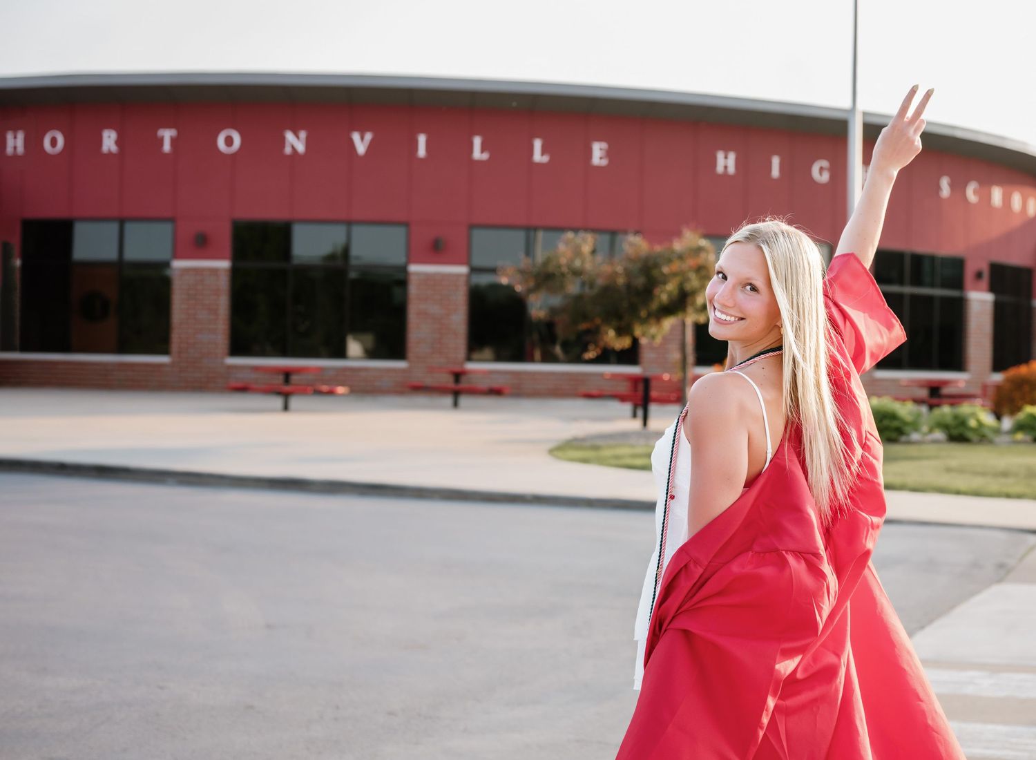 A person in a bright red dress twirls gracefully in front of a brick building on a sunny day.