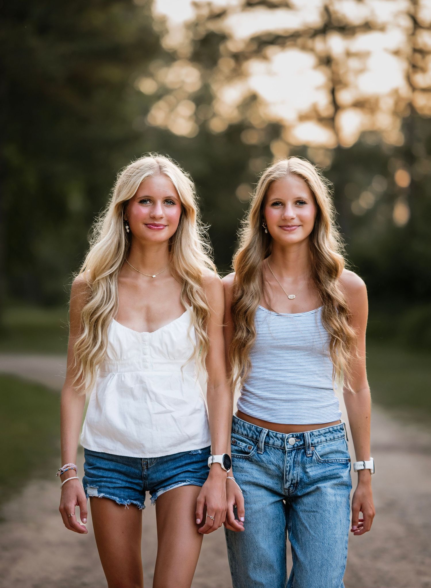 Two people wearing casual summer outfits of denim shorts and white tops pose together outdoors at sunset.