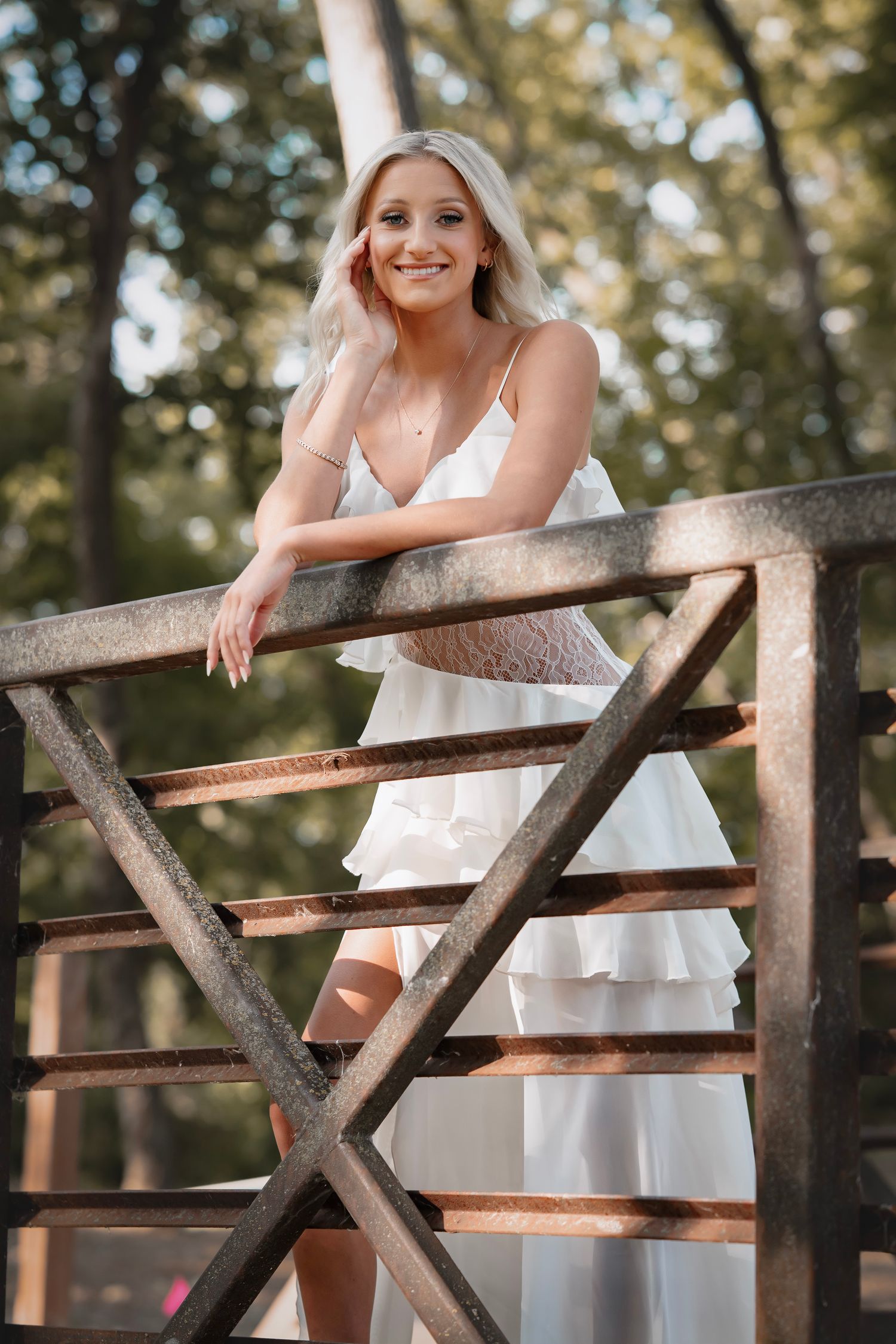 A person in a white summer dress poses along a rustic wooden fence in a sunlit outdoor setting.
