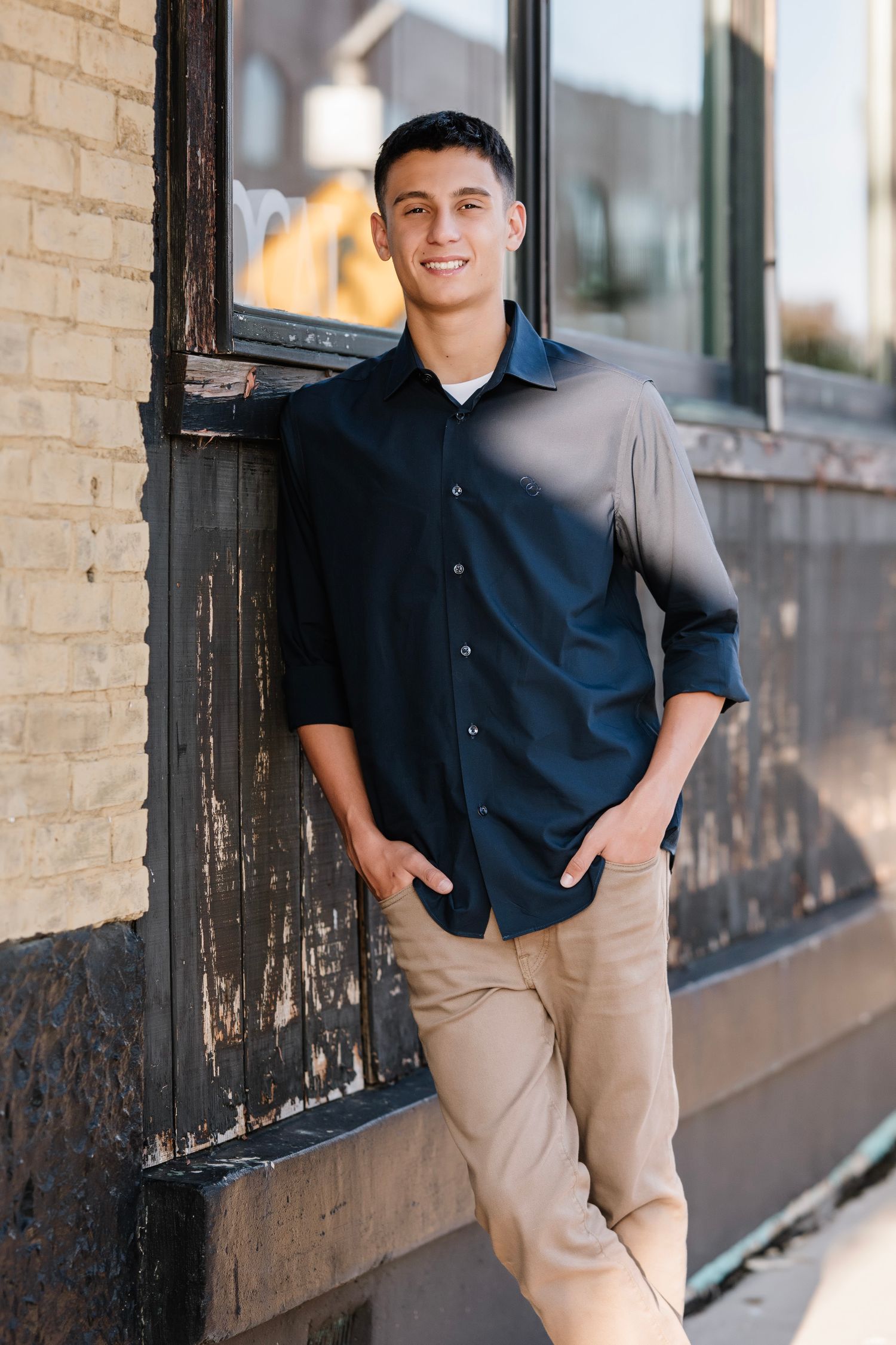 Professional outdoor portrait session showing a person in a navy button-down shirt and khaki shorts against a brick wall.