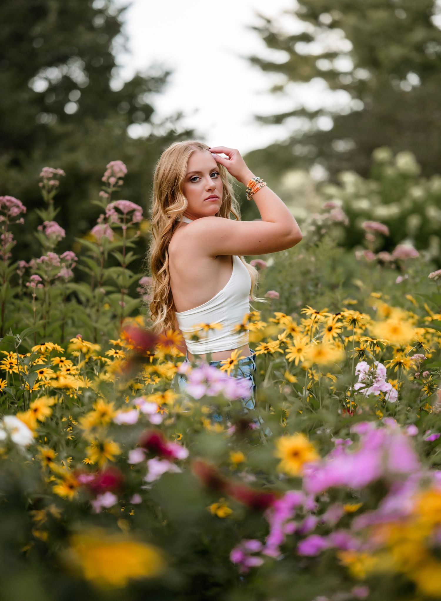 A person poses gracefully in a vibrant wildflower meadow filled with yellow and purple blooms on a summer day.