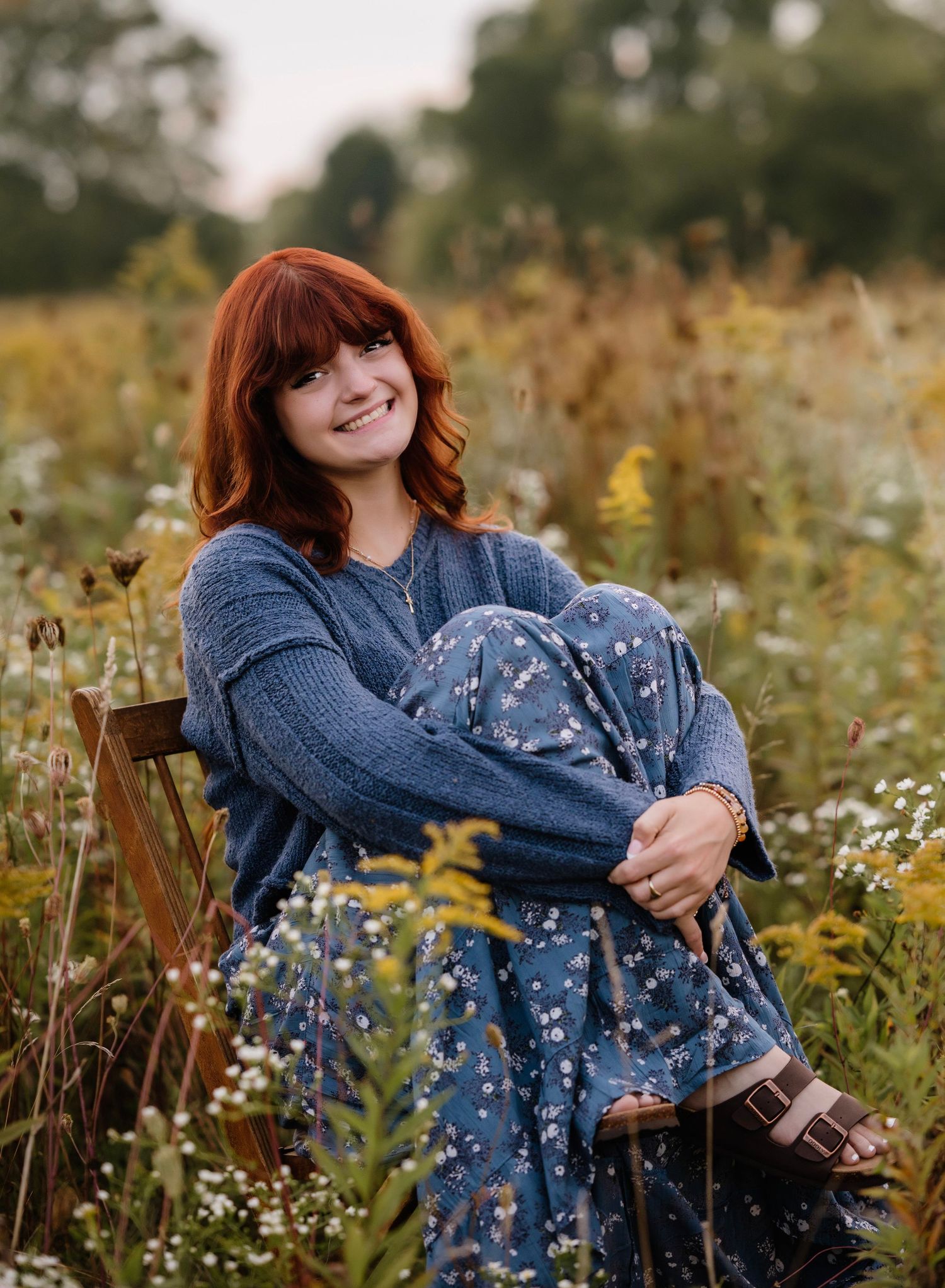 Person in denim jacket poses in a wildflower meadow with white and yellow blooms during golden hour.