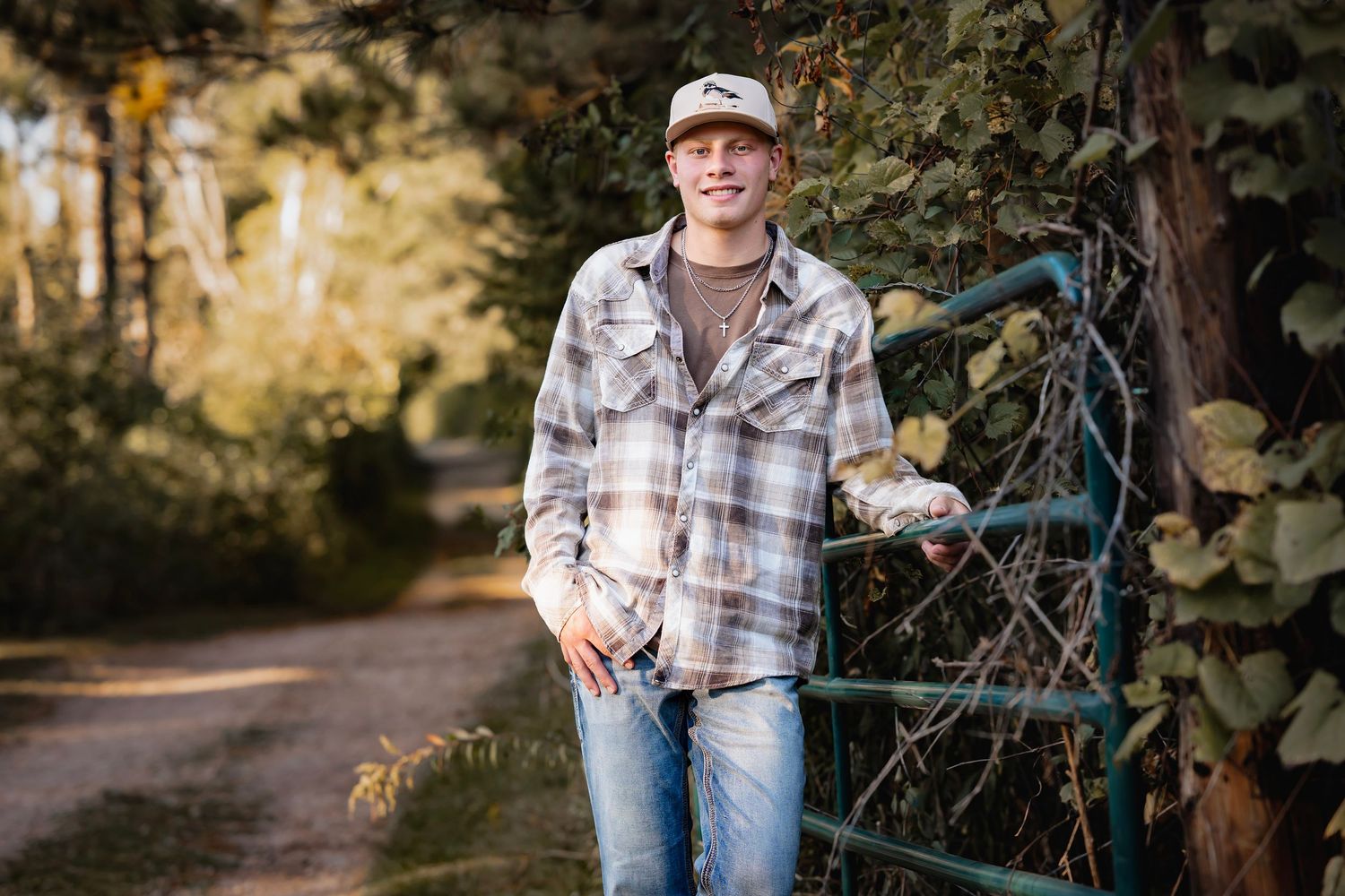 Person in plaid shirt and jeans poses outdoors in autumn forest setting during golden hour photography session.