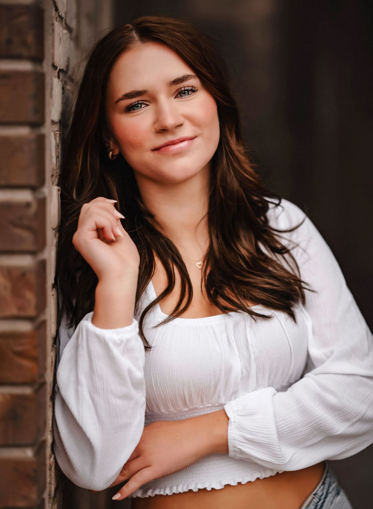 Lifestyle portrait series showing casual poses against a rustic brick wall in a white blouse.