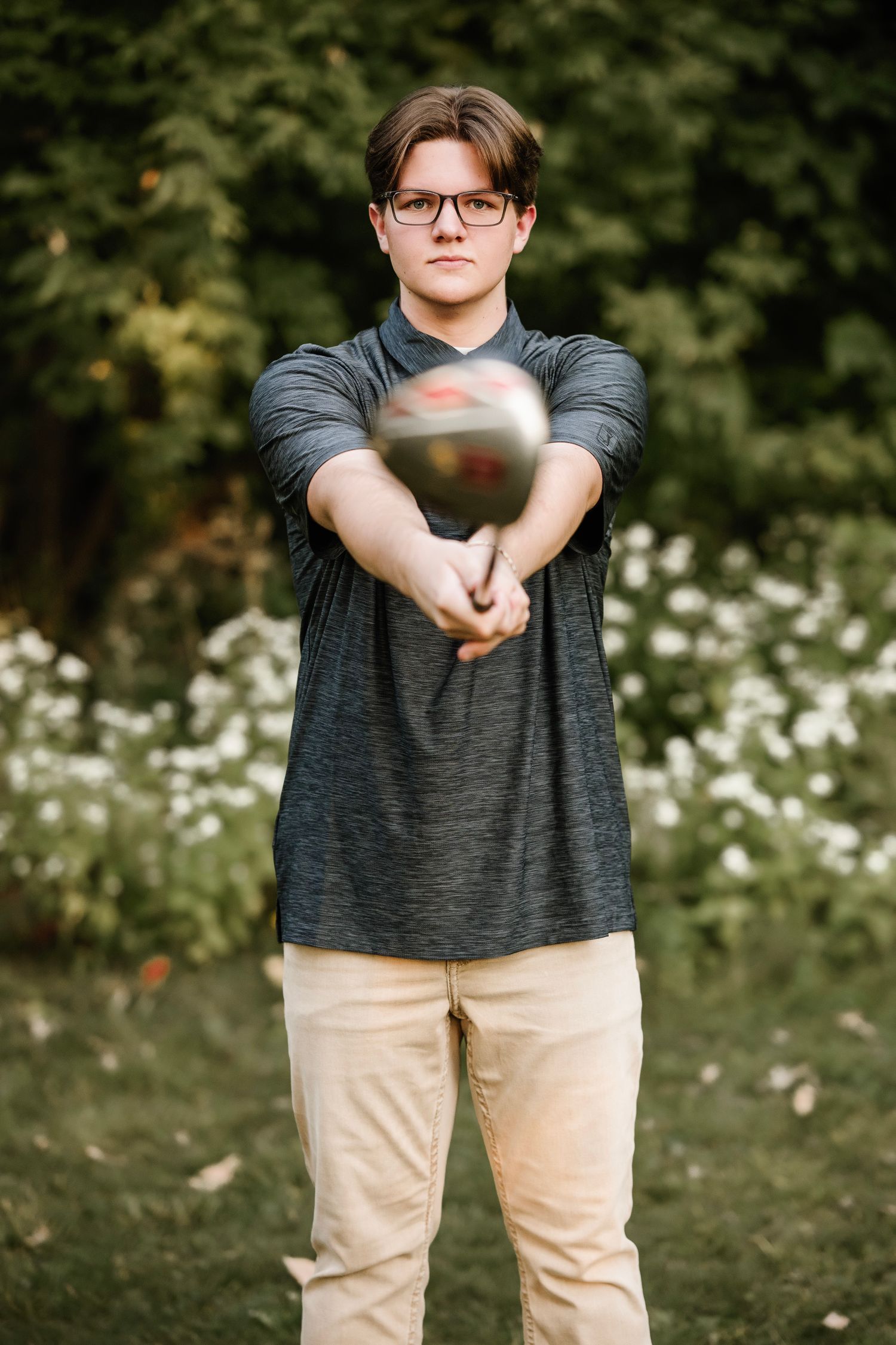 A person in glasses and a dark t-shirt stands in a grassy field with white wildflowers in the background.