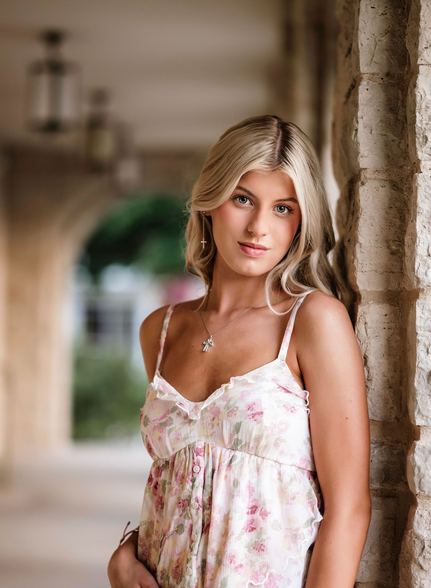 Portrait of someone wearing a white floral summer dress while standing in an elegant arched stone corridor.