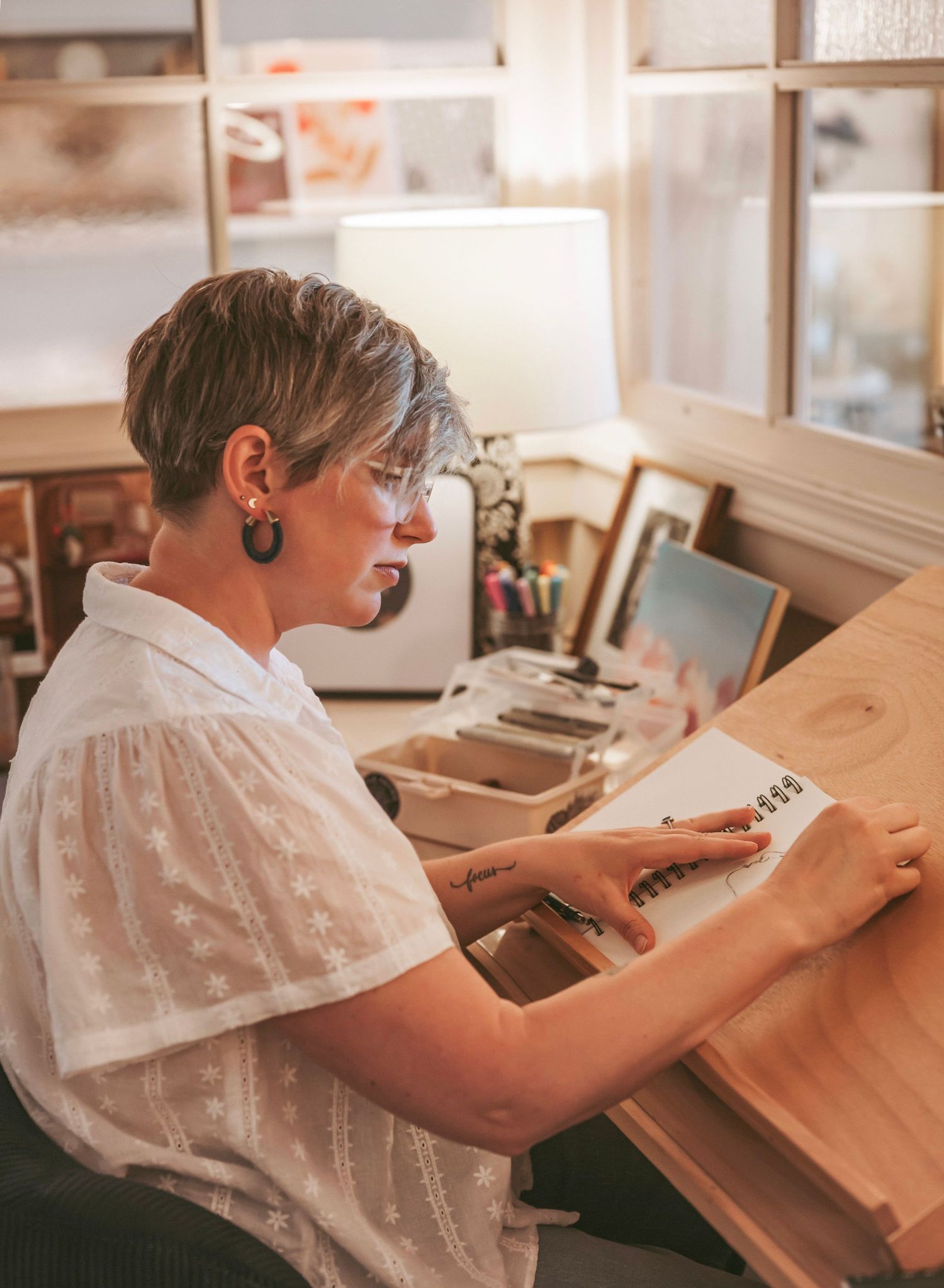 A person wearing headphones works at a wooden drafting desk in a bright office space.