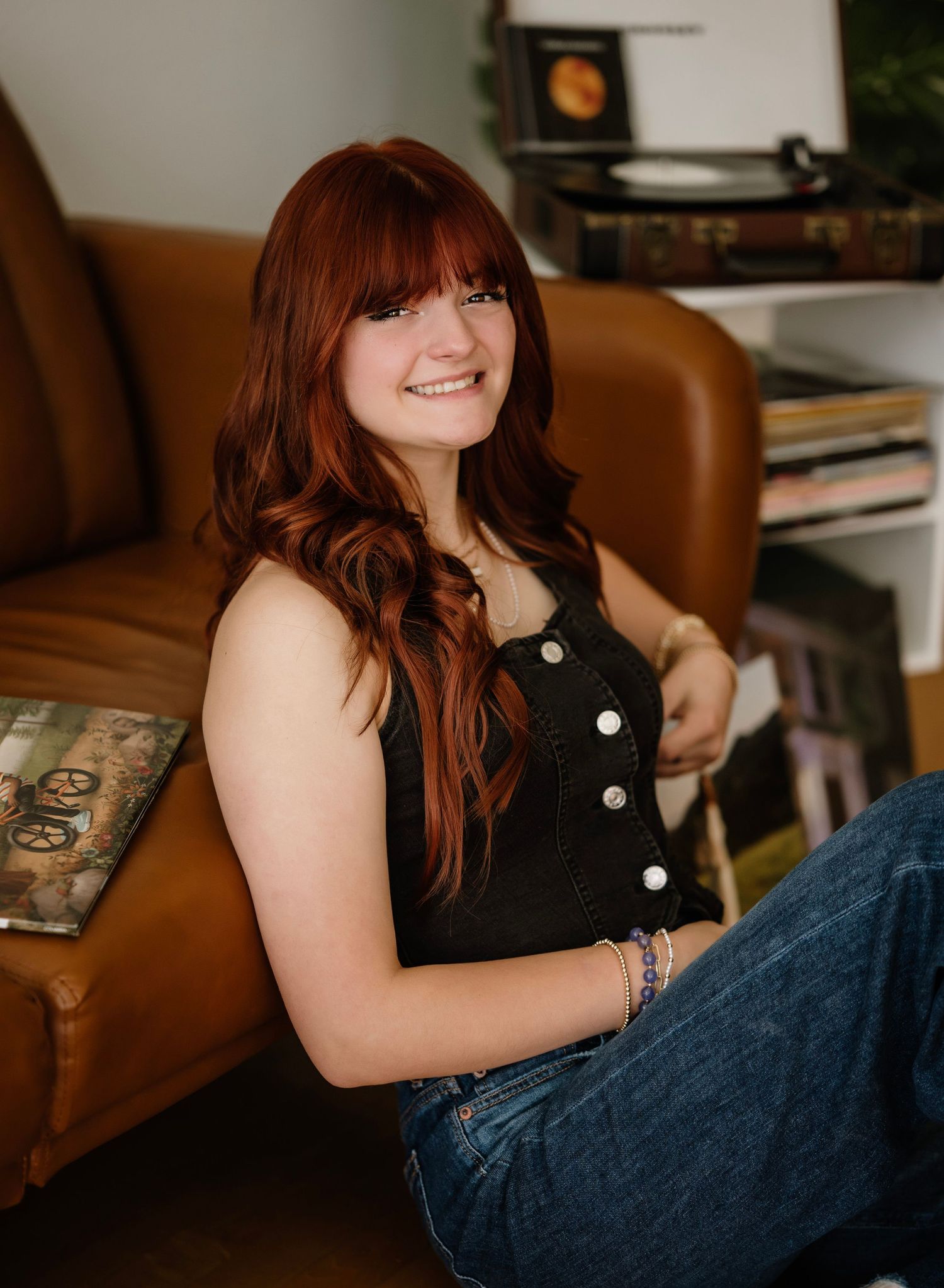 A person in a black sleeveless top lounges comfortably on a brown leather couch in a cozy home setting.
