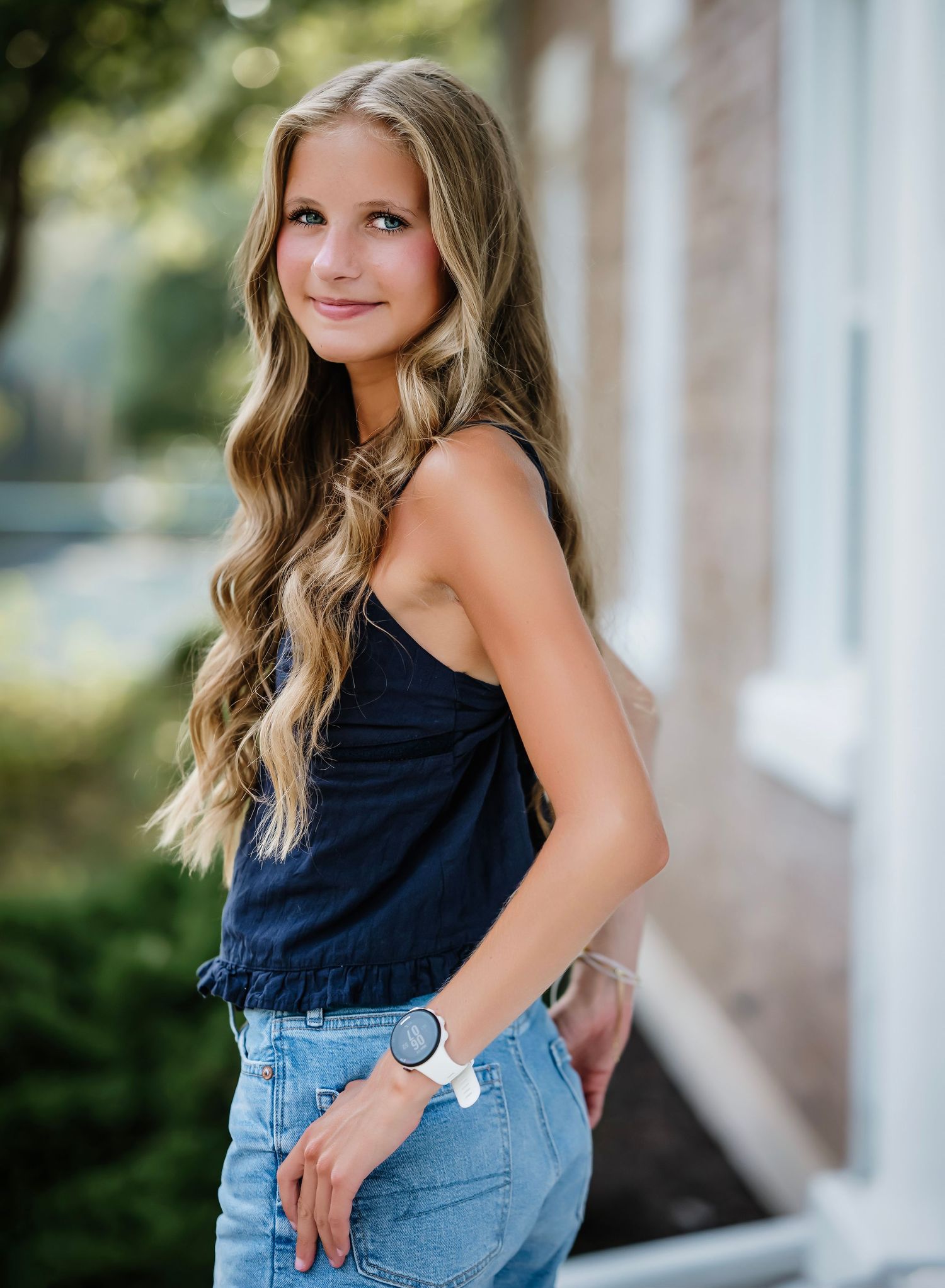 Person wearing a navy sleeveless top and light denim jeans poses outdoors against a blurred background.