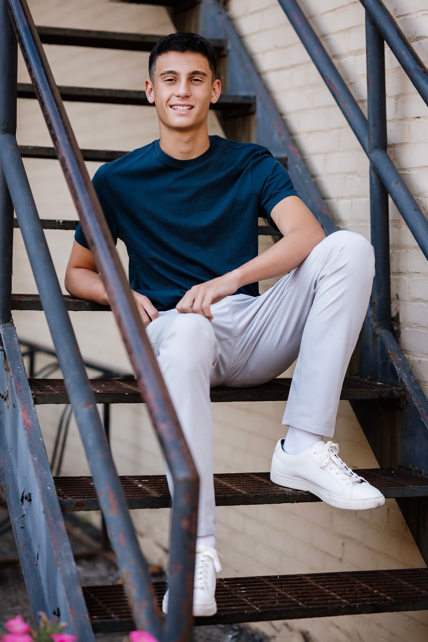 Three people in navy shirts and light pants sitting casually on outdoor wooden stairs.