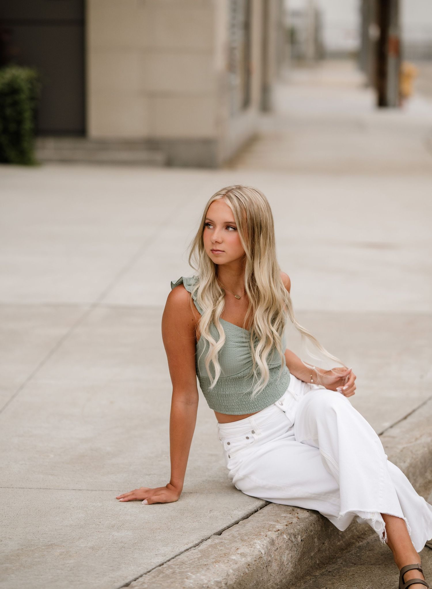 Someone in a sage green top and white pants poses on concrete steps.