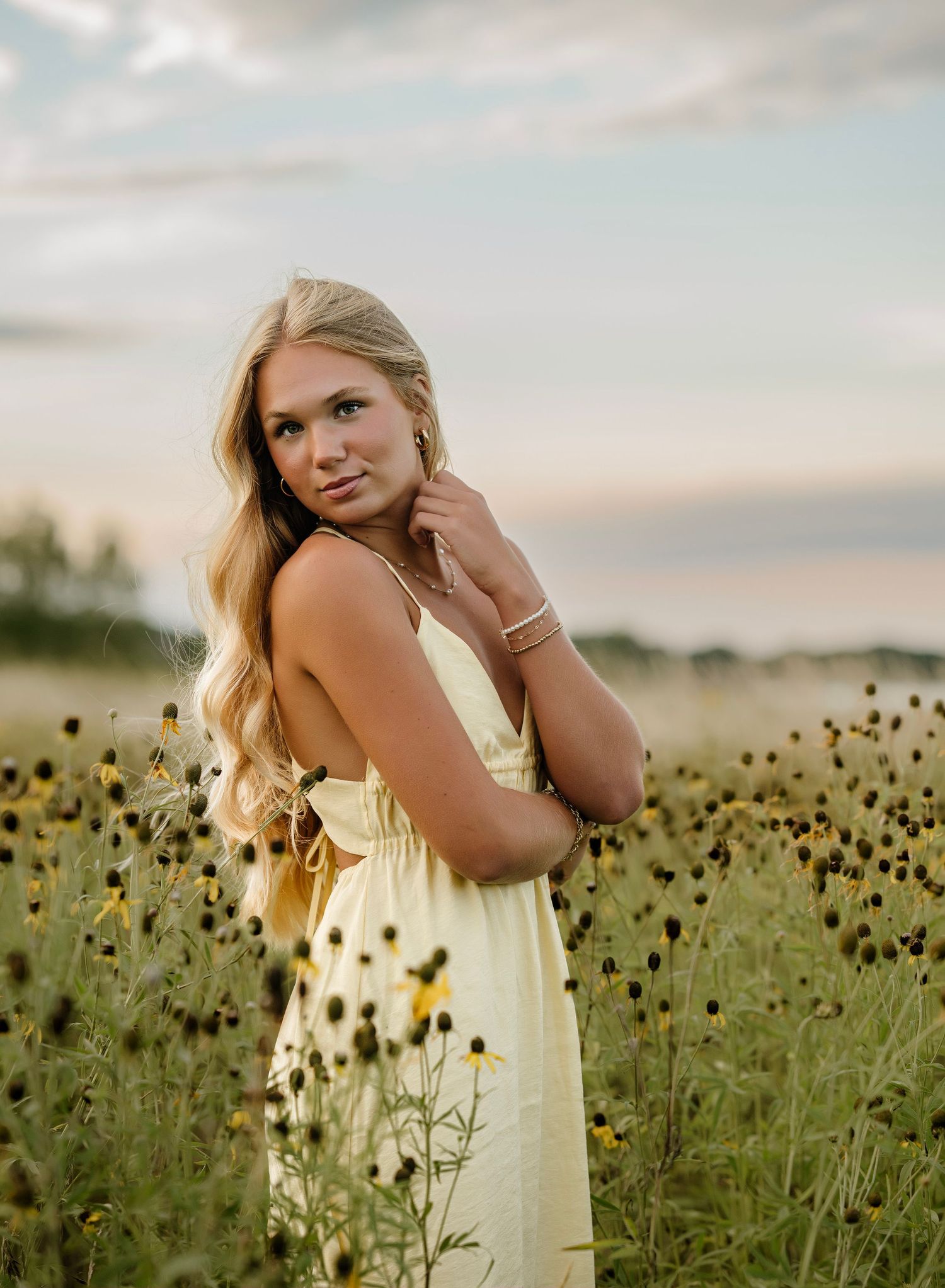 A person in a pale yellow dress poses gracefully among tall black-eyed susan wildflowers at sunset.