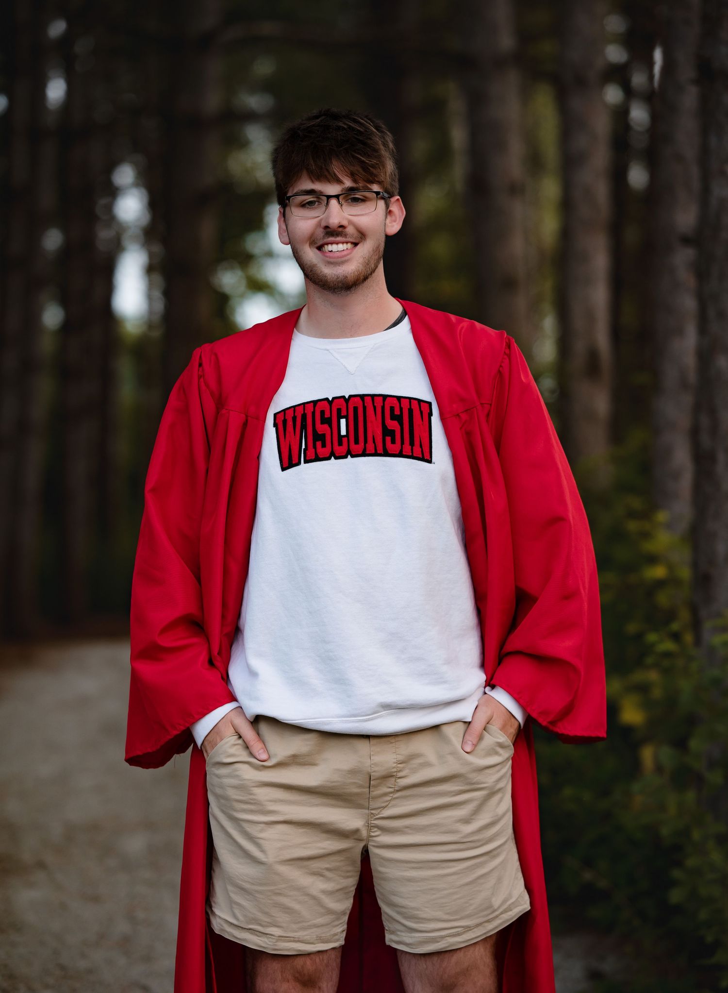 A person wearing a red cardigan and khaki shorts stands in a wooded outdoor setting.