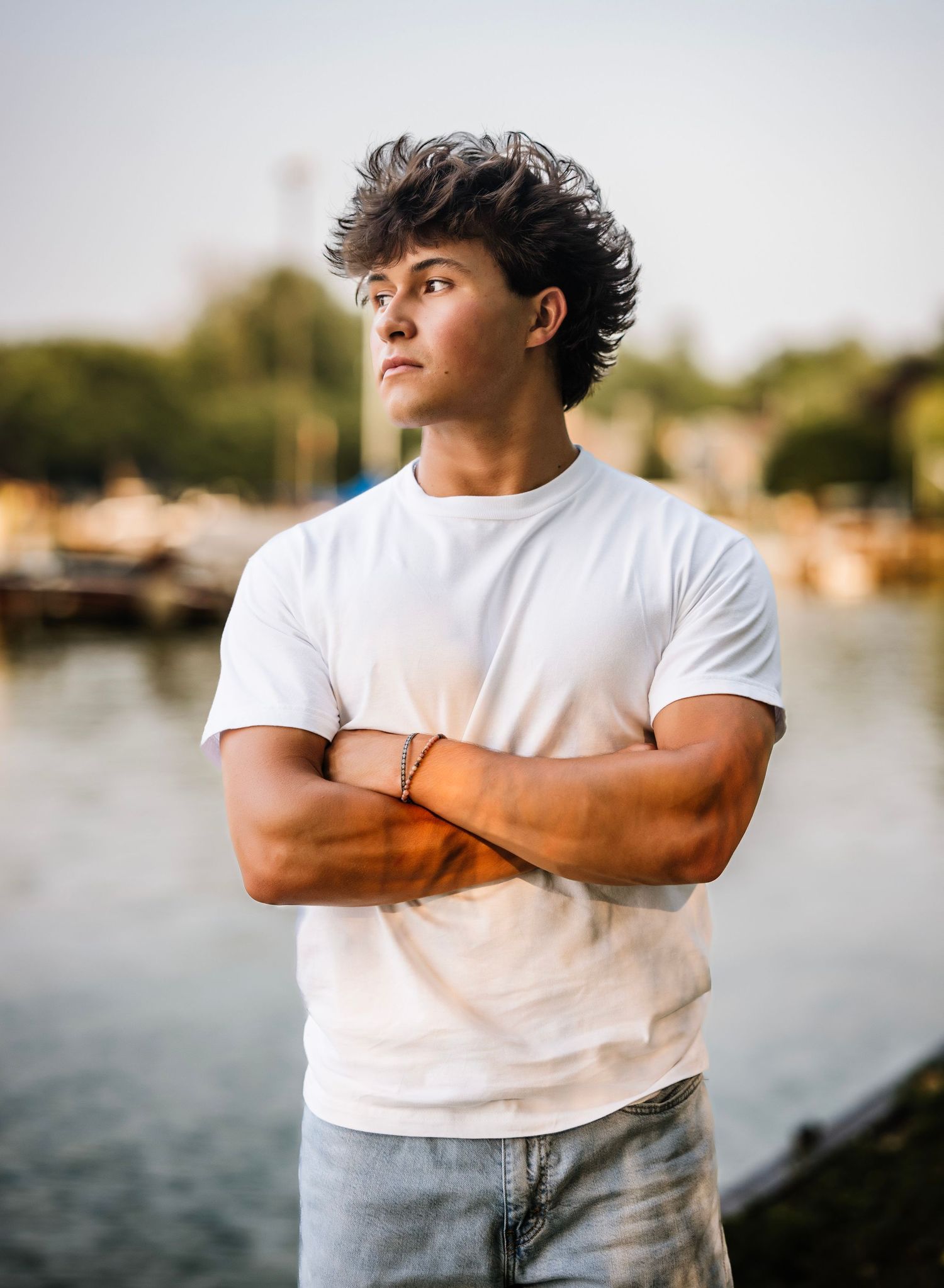 A person in a white t-shirt poses against a waterfront backdrop during golden hour.