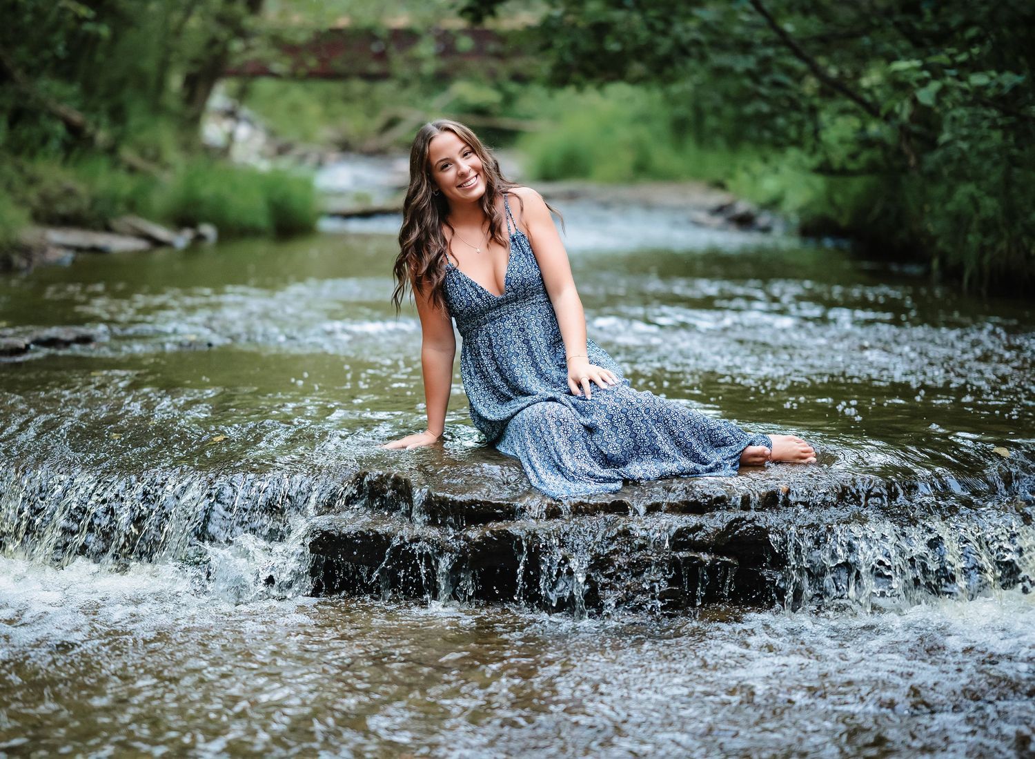 Someone in a blue dress reclines on wet rocks as water cascades around them.