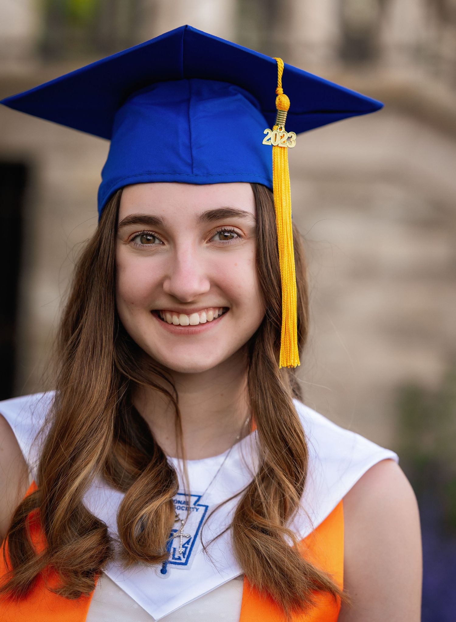 Graduate in blue cap and gown with yellow tassel poses for series of celebratory portraits against blurred background.