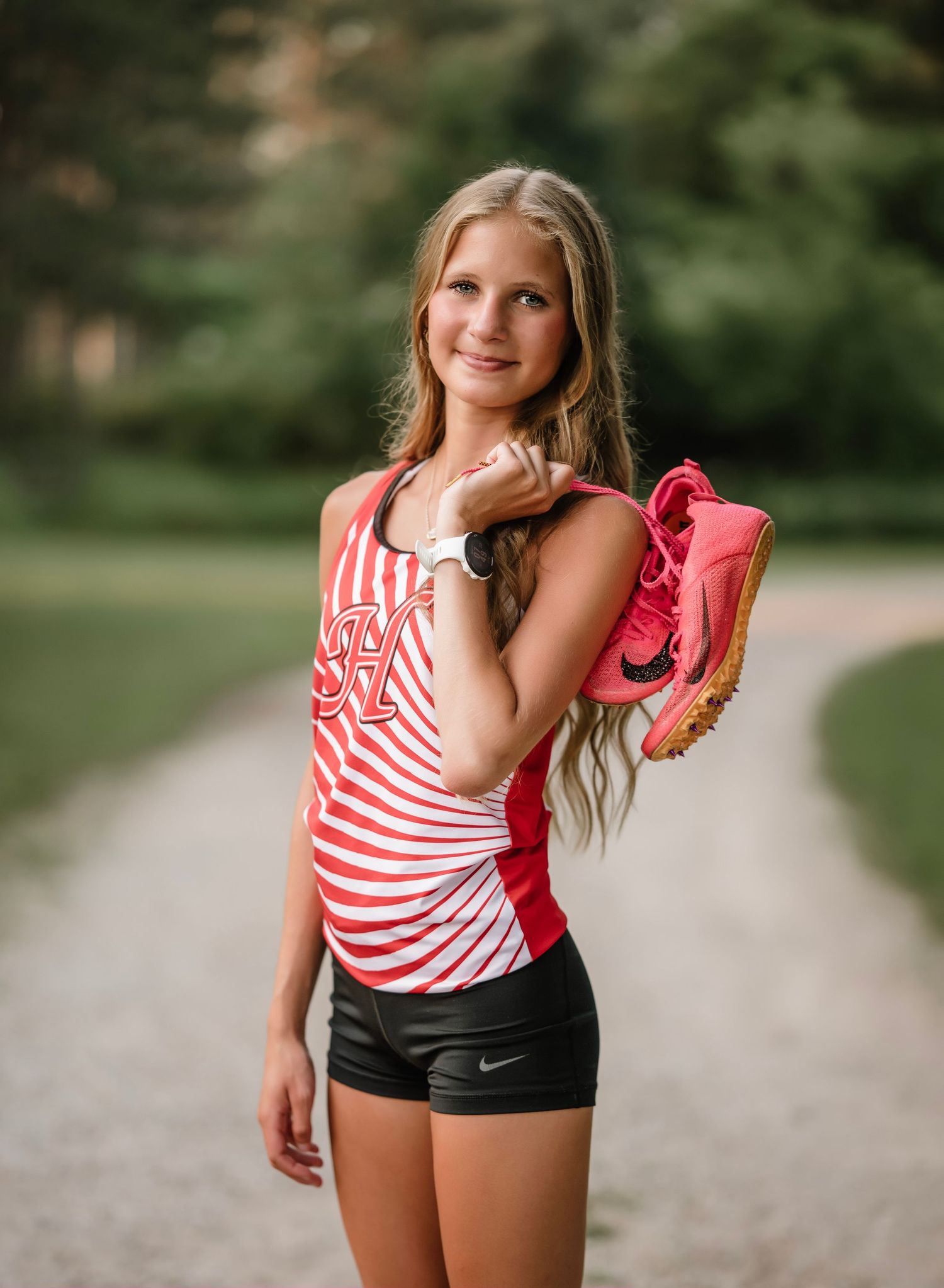 A person in a red and white striped tank top and black shorts poses outdoors on a gravel path.