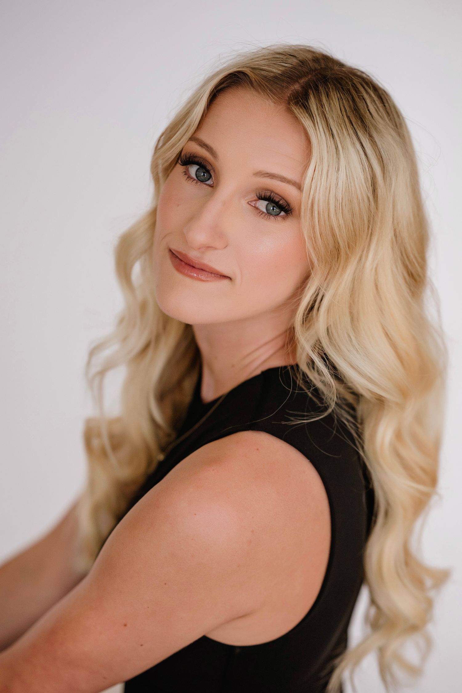 A high school senior with blue eyes and wavy hair poses in a black sleeveless top against a white background.