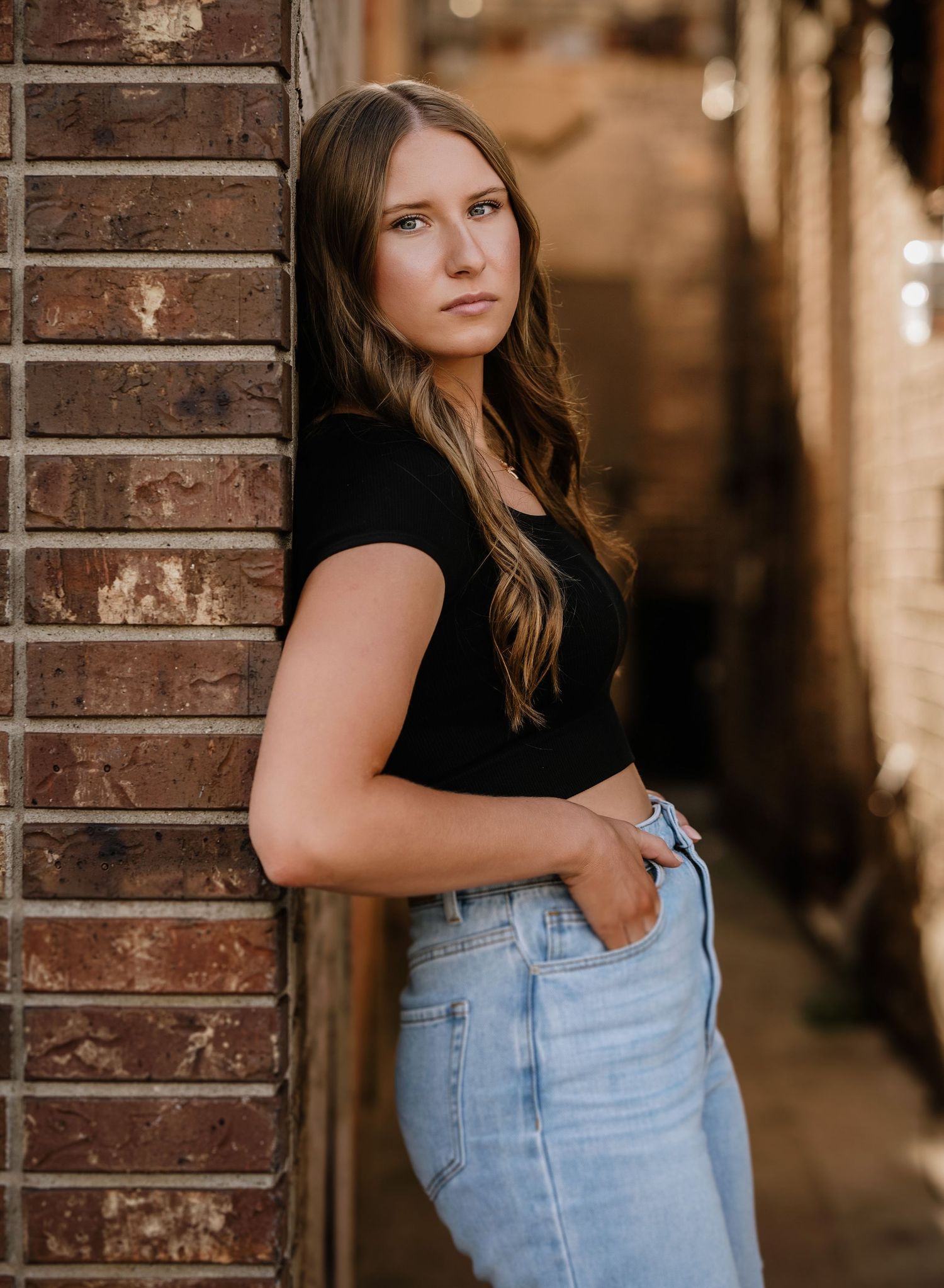 Moody portrait series against rustic brick wall wearing casual denim and dark top.