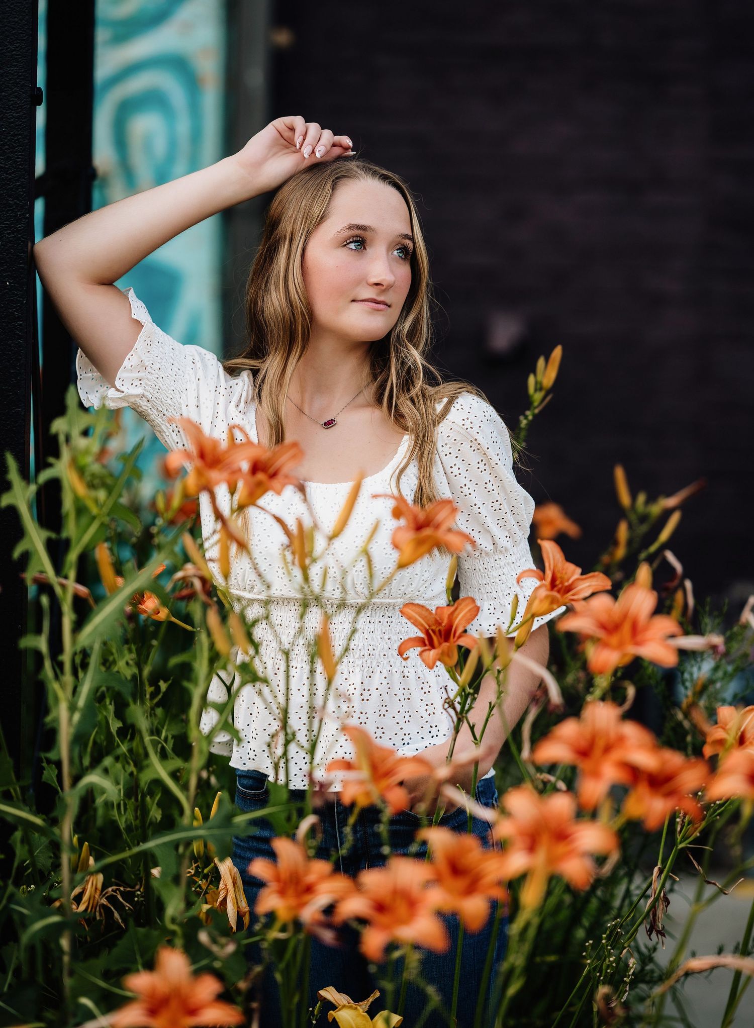 A white eyelet lace top stands out against vibrant orange lilies in a summer portrait setting.