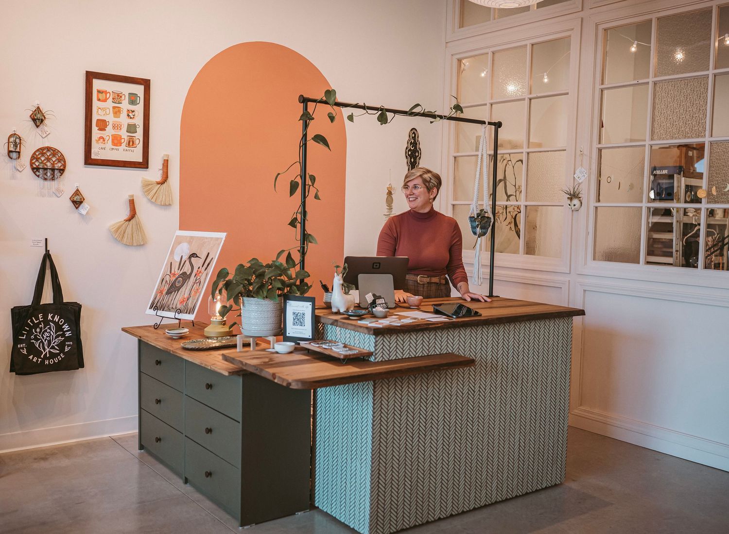 A cozy retail shop interior with sage green counter, coral accent wall, and vintage-style decor elements.