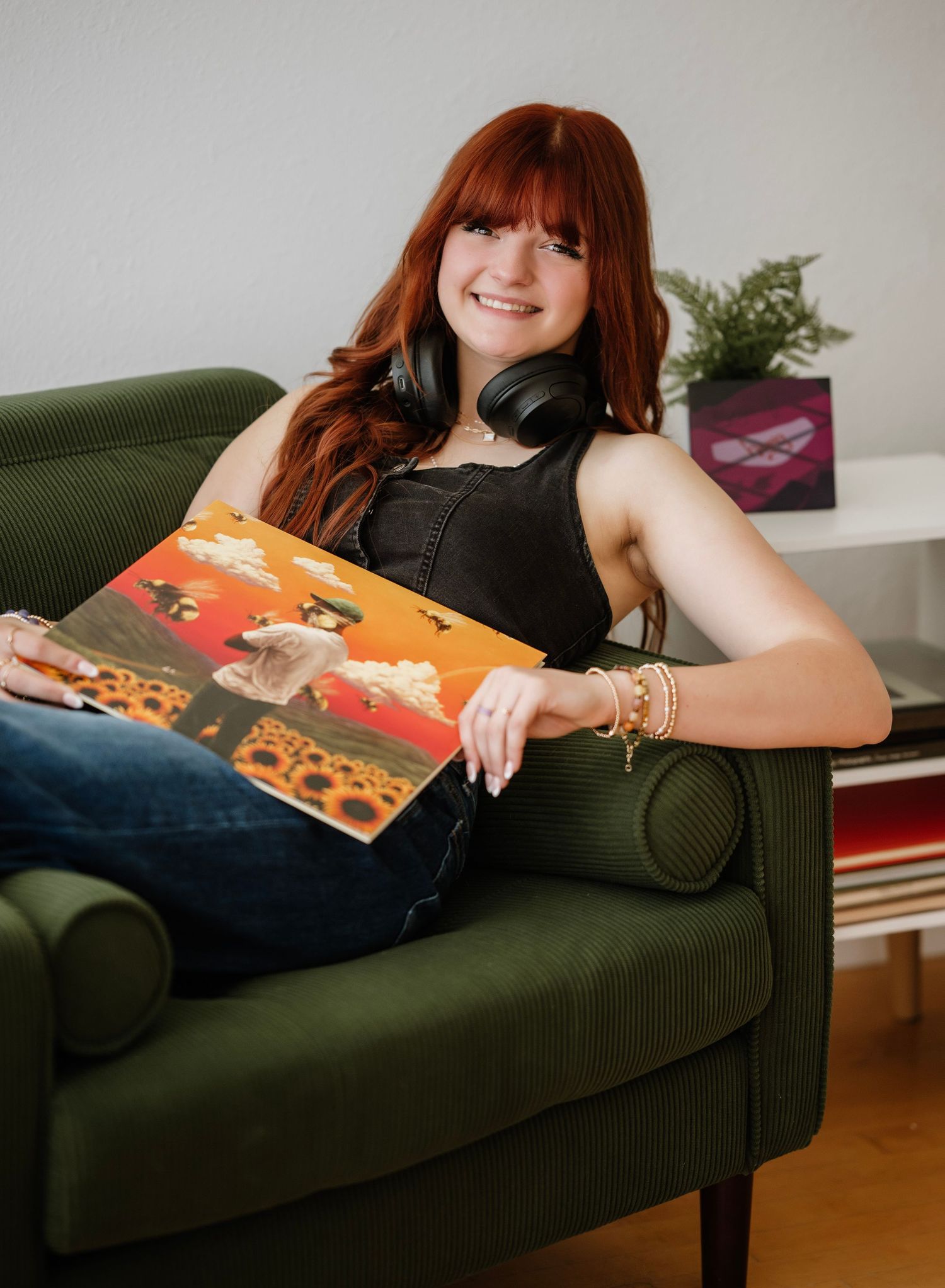 A person with red hair lounges on a dark couch while holding a vinyl record album.