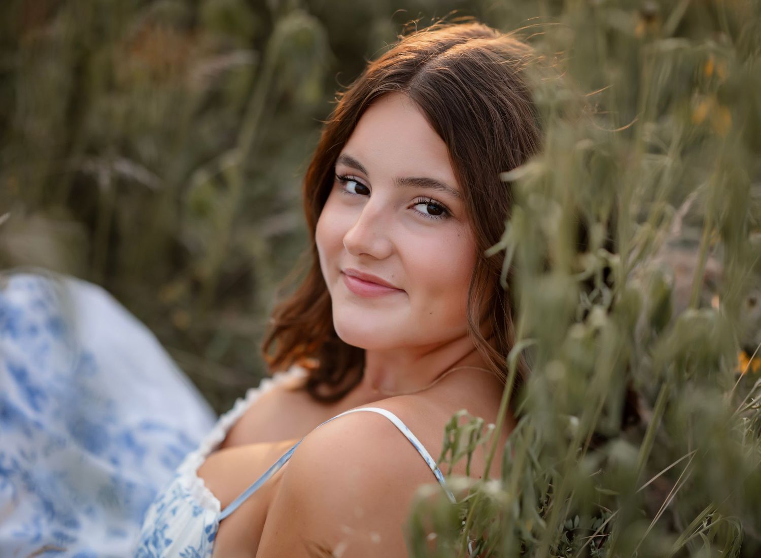 A portrait in a meadow shows someone in a white dress surrounded by tall grass and wildflowers at sunset.