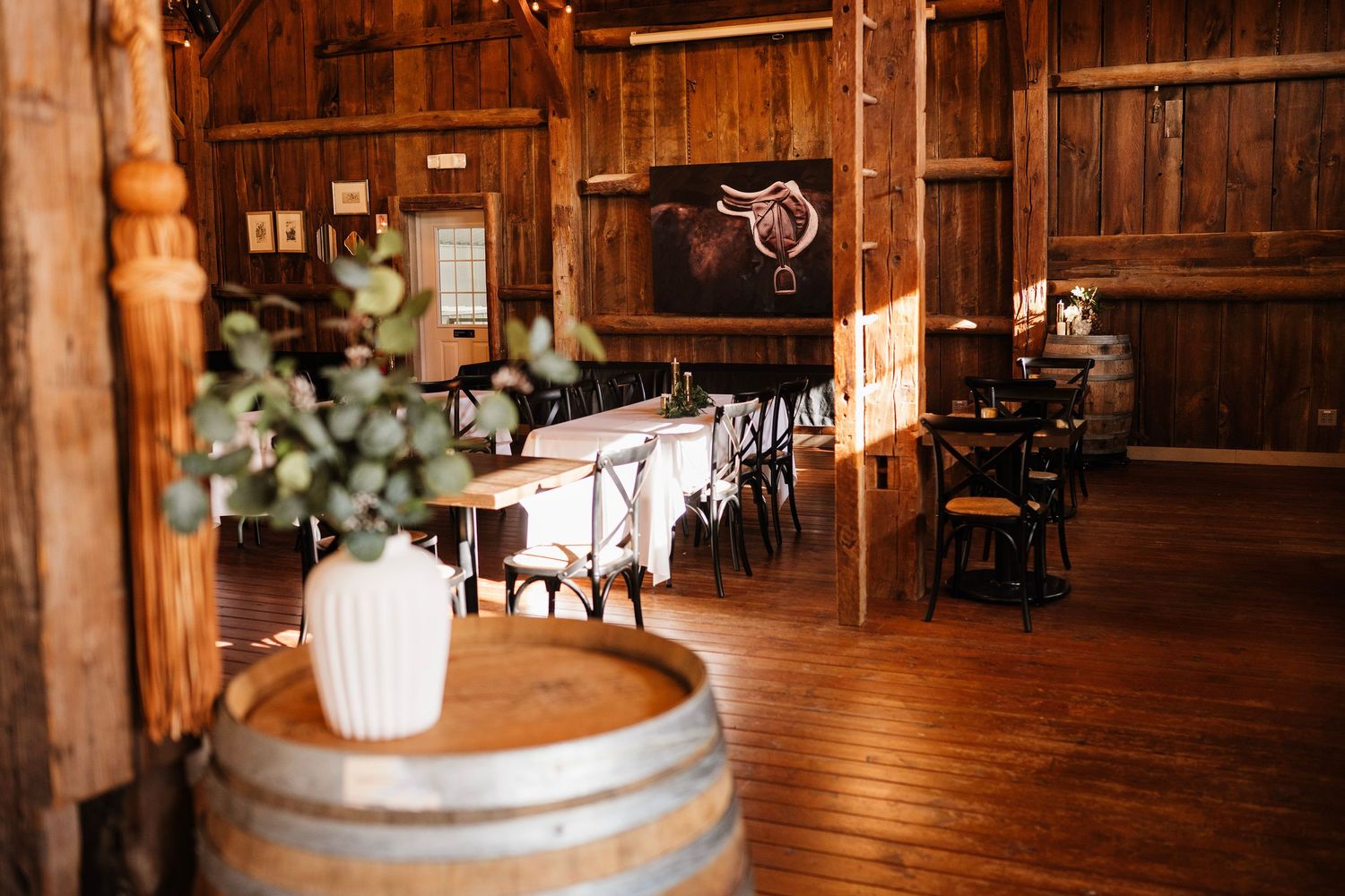 Rustic barn wedding venue with wooden barrels, white floral centerpieces, and elegant table settings.