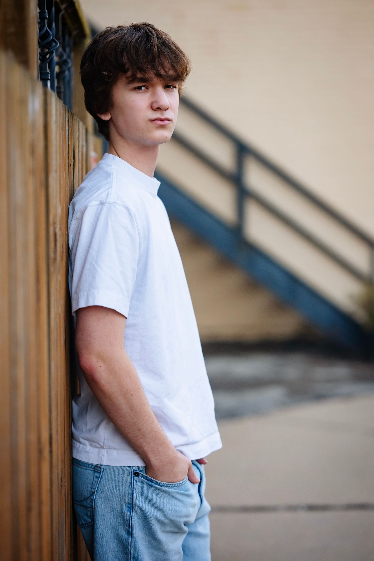 Person in a white t-shirt and light blue jeans stands against a beige wall with architectural details in the background.