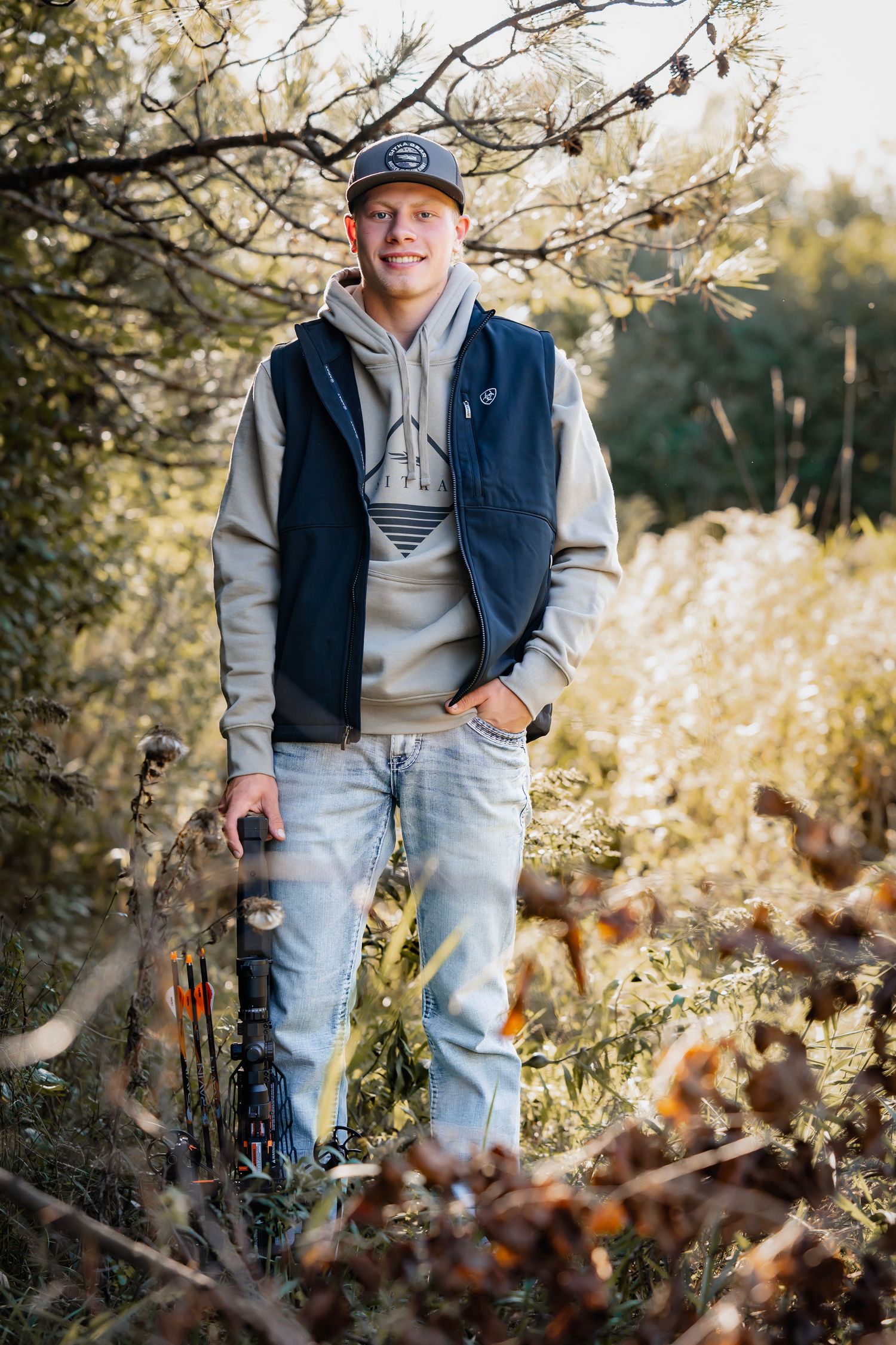 A series of outdoor autumn portraits showing someone wearing a navy vest and baseball cap among fall foliage.