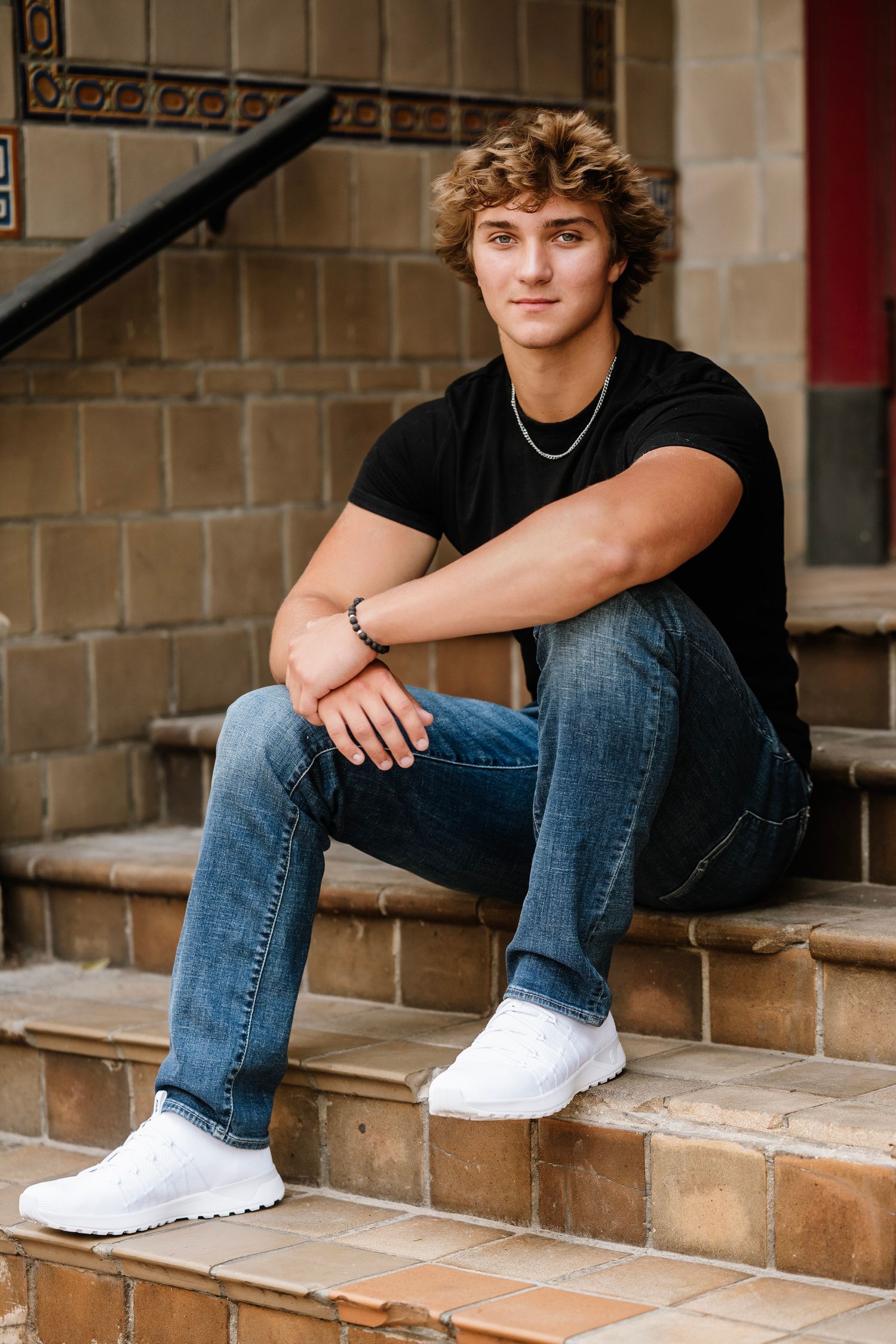 Person wearing jeans and white sneakers sits casually on brick steps in a relaxed outdoor setting.