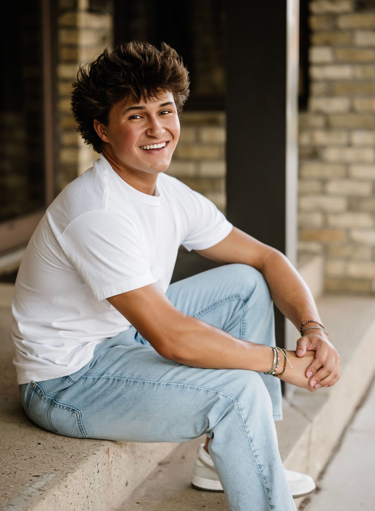 Person in white t-shirt and light jeans sits casually on concrete surface in outdoor setting.