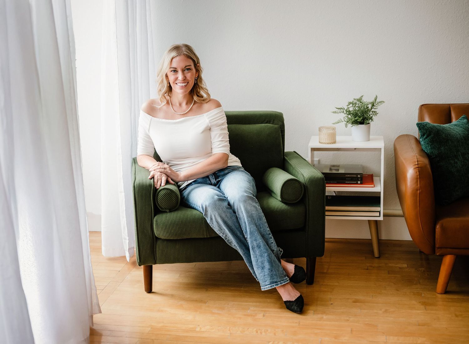 Woman relaxes in green armchair by window with natural light in modern minimalist living room interior.
