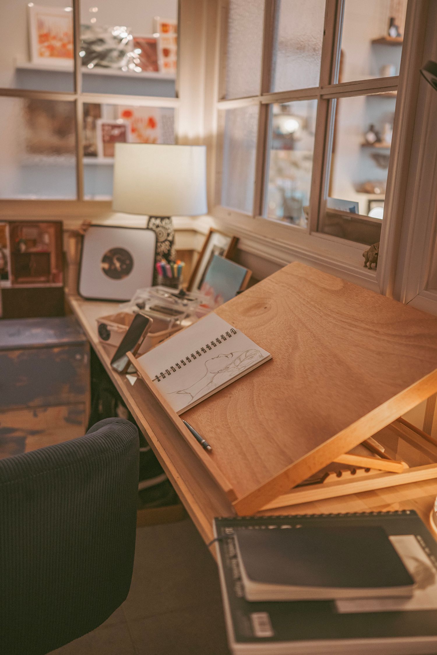 Wooden desk with angled writing surface shown in multiple positions against dark green background in gallery setting.