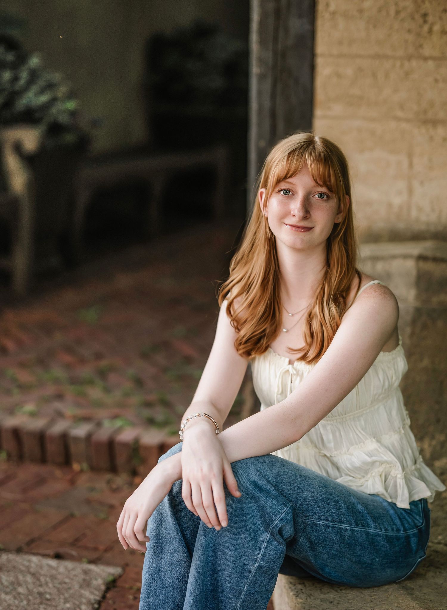 A person in a white top and blue jeans sits casually on stone steps outdoors in a natural setting.