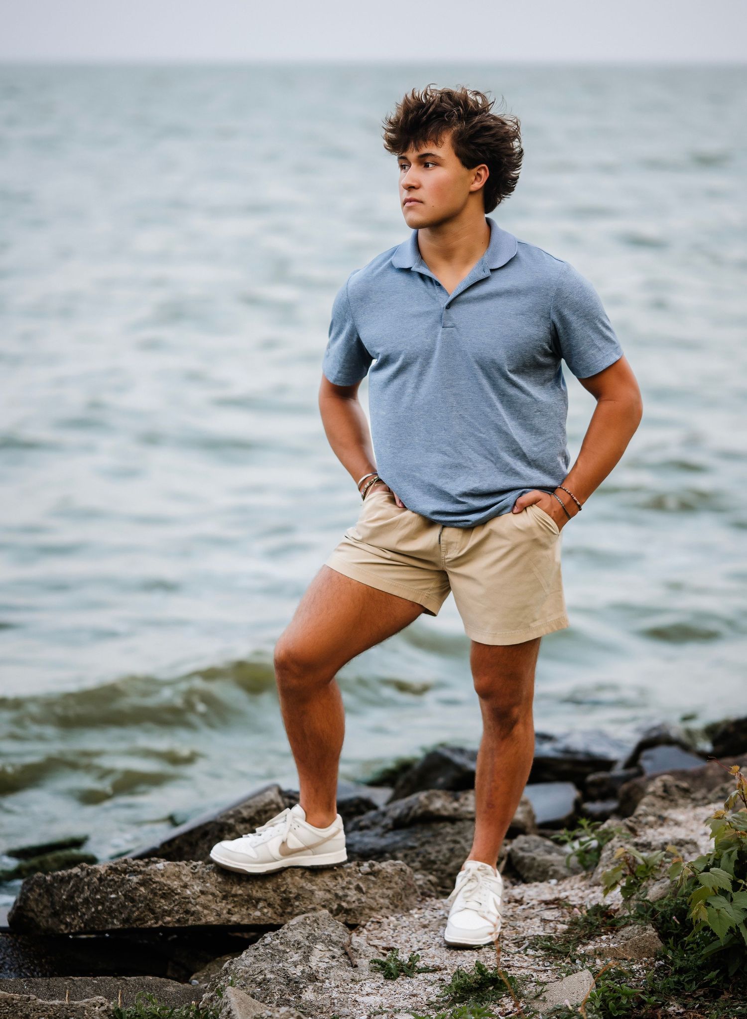 Three photos show someone in a gray polo shirt and khaki shorts posing on rocky coastal terrain near the water.