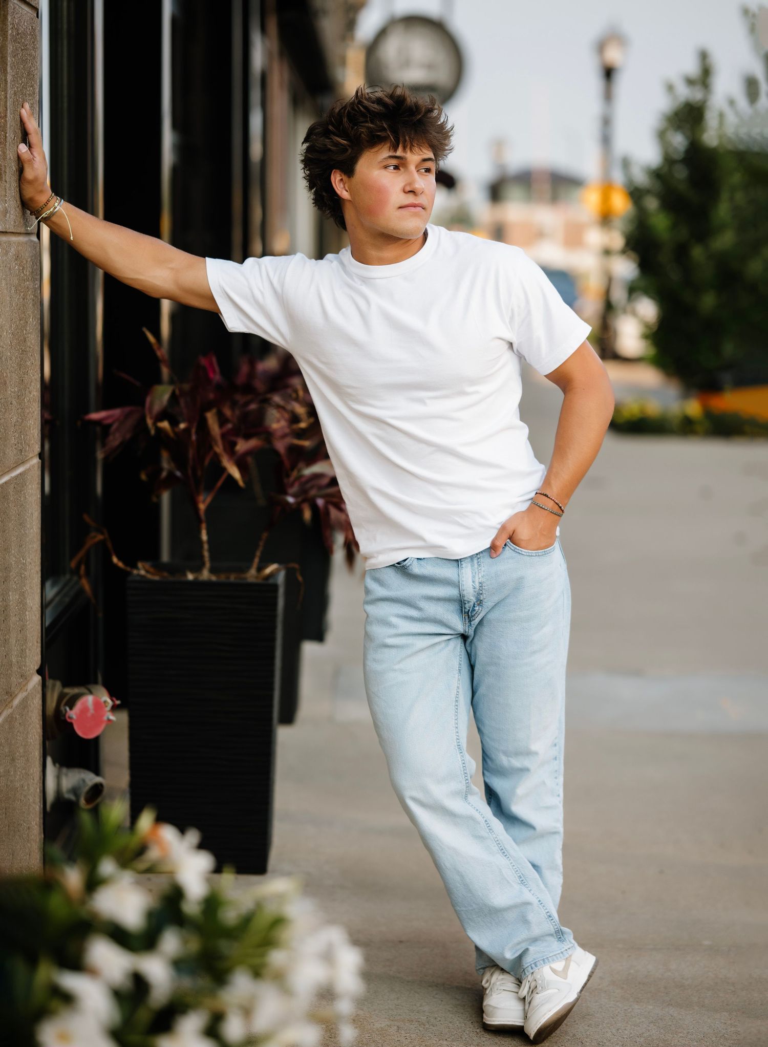 Person in white t-shirt and light jeans performs expressive dance moves on urban sidewalk.