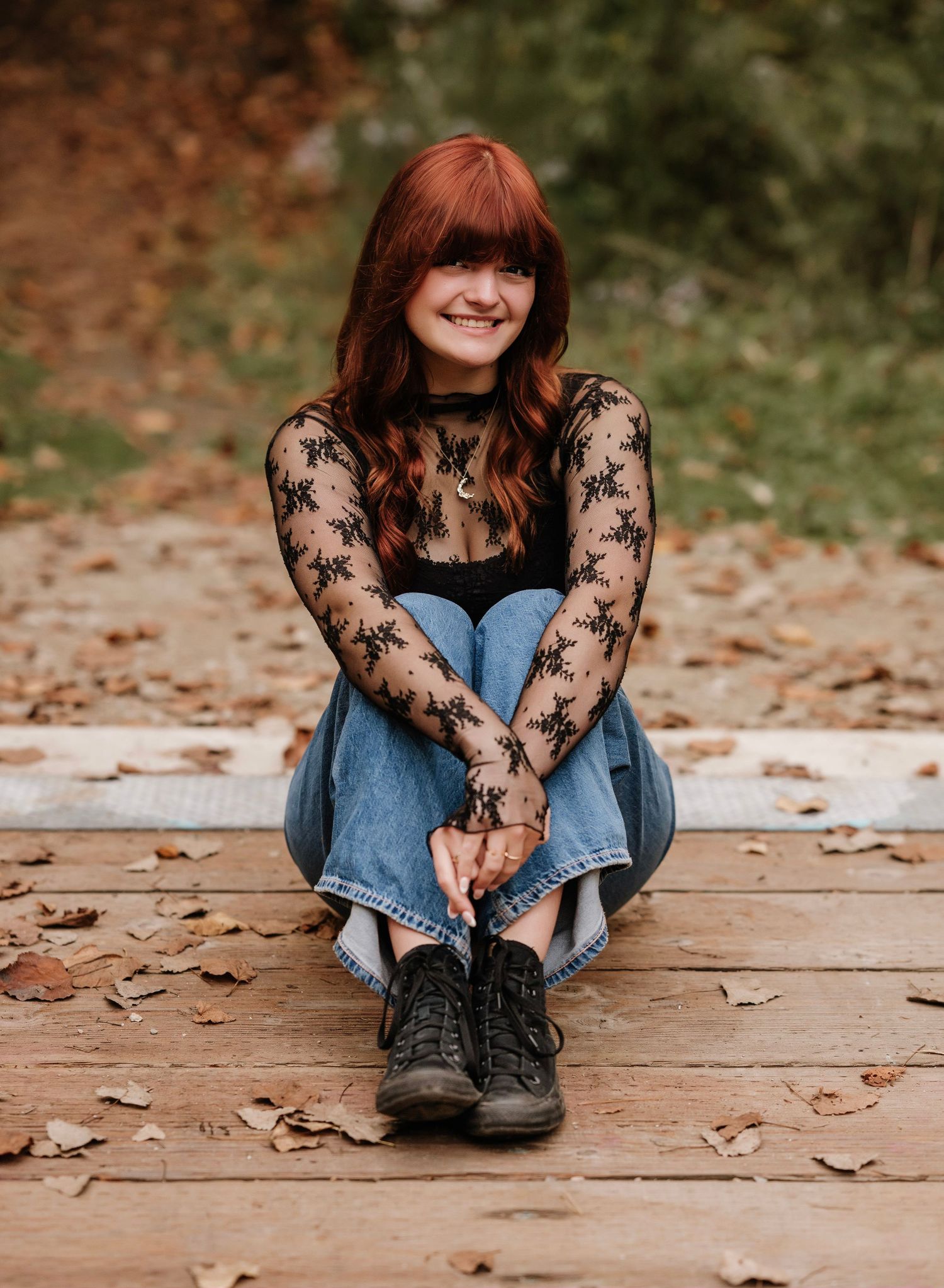 A person wearing a lace sleeve top and denim dress sits on wooden steps covered in autumn leaves.