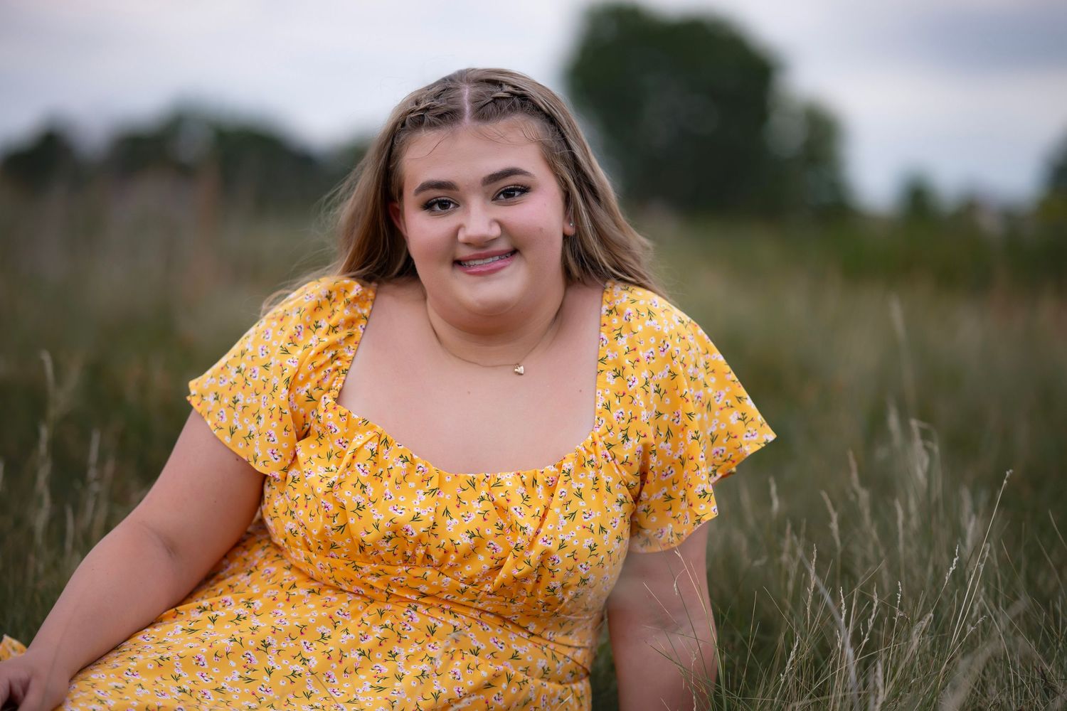 Young woman in yellow floral dress smiling in a golden field during a senior portrait photography session.