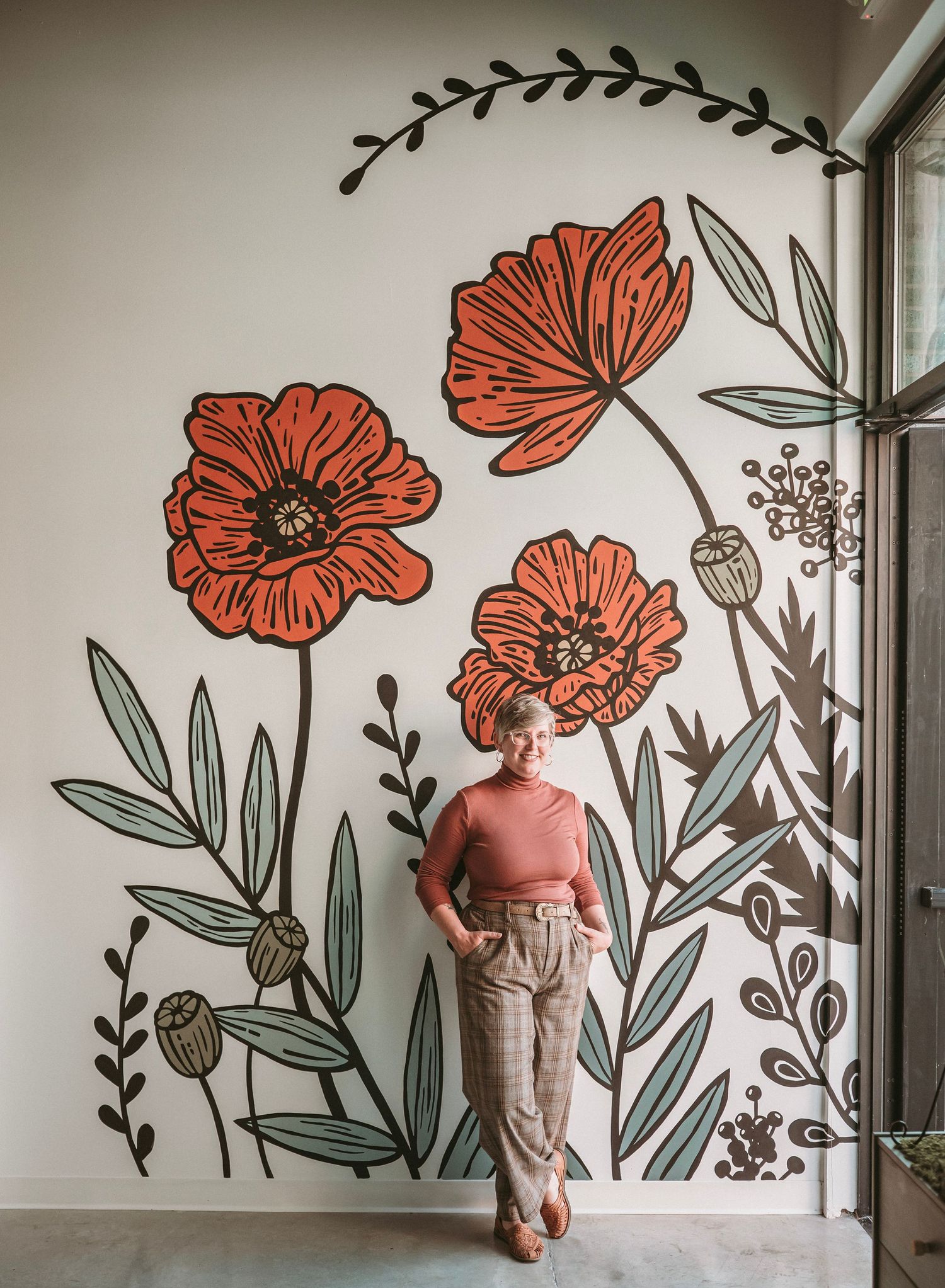 A large floral mural featuring red poppies and botanical elements painted on a white interior wall.