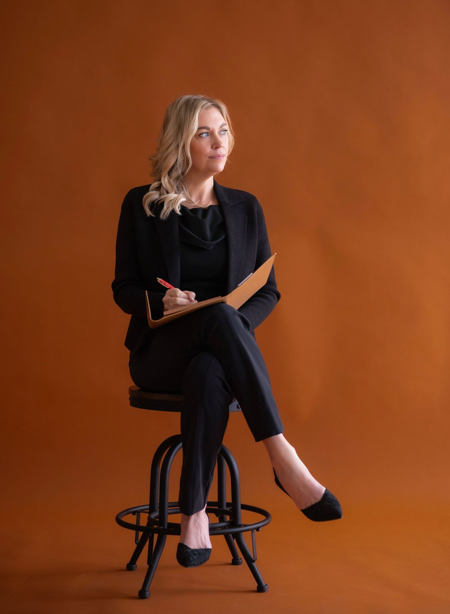 Studio branding portraits on a black stool against orange backdrop wearing business casual attire.