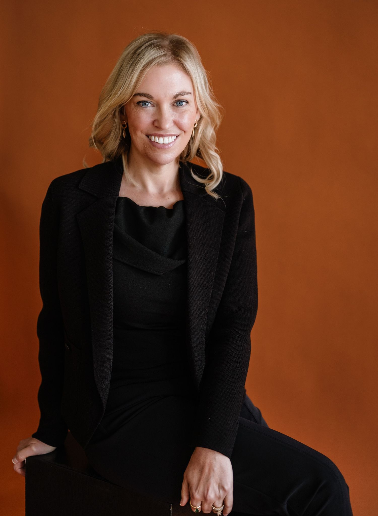 Studio portraits against terracotta backdrop wearing elegant black blazer.