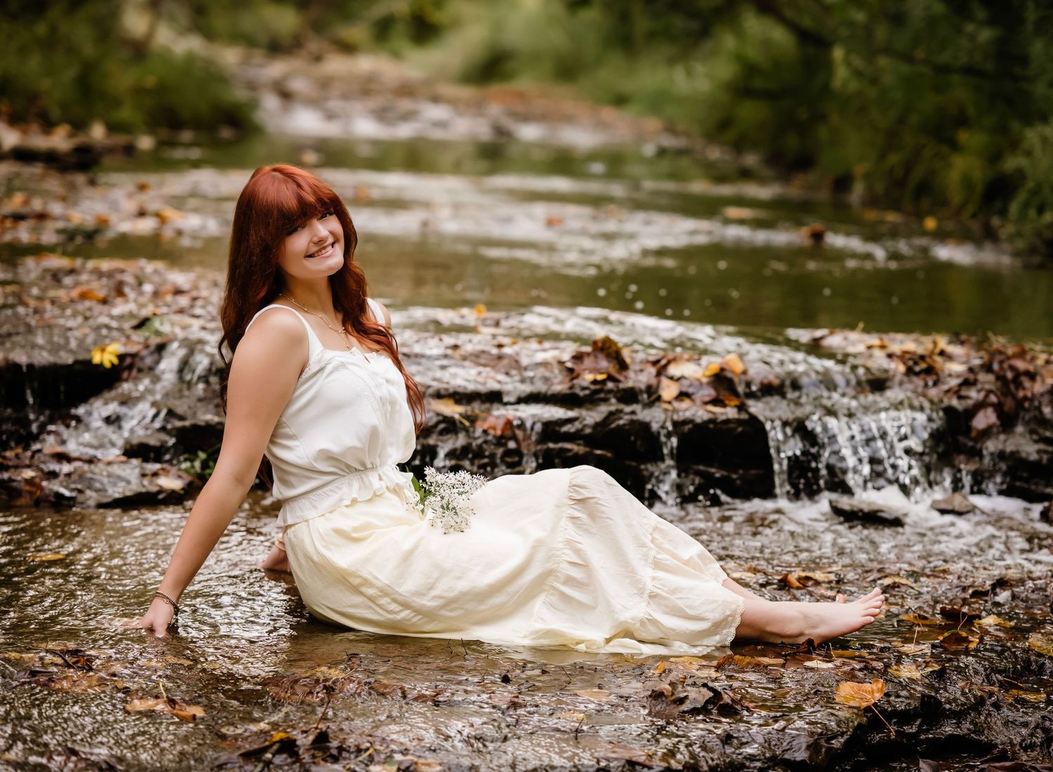A white dress flows gracefully along a rocky riverbank in a natural outdoor setting.