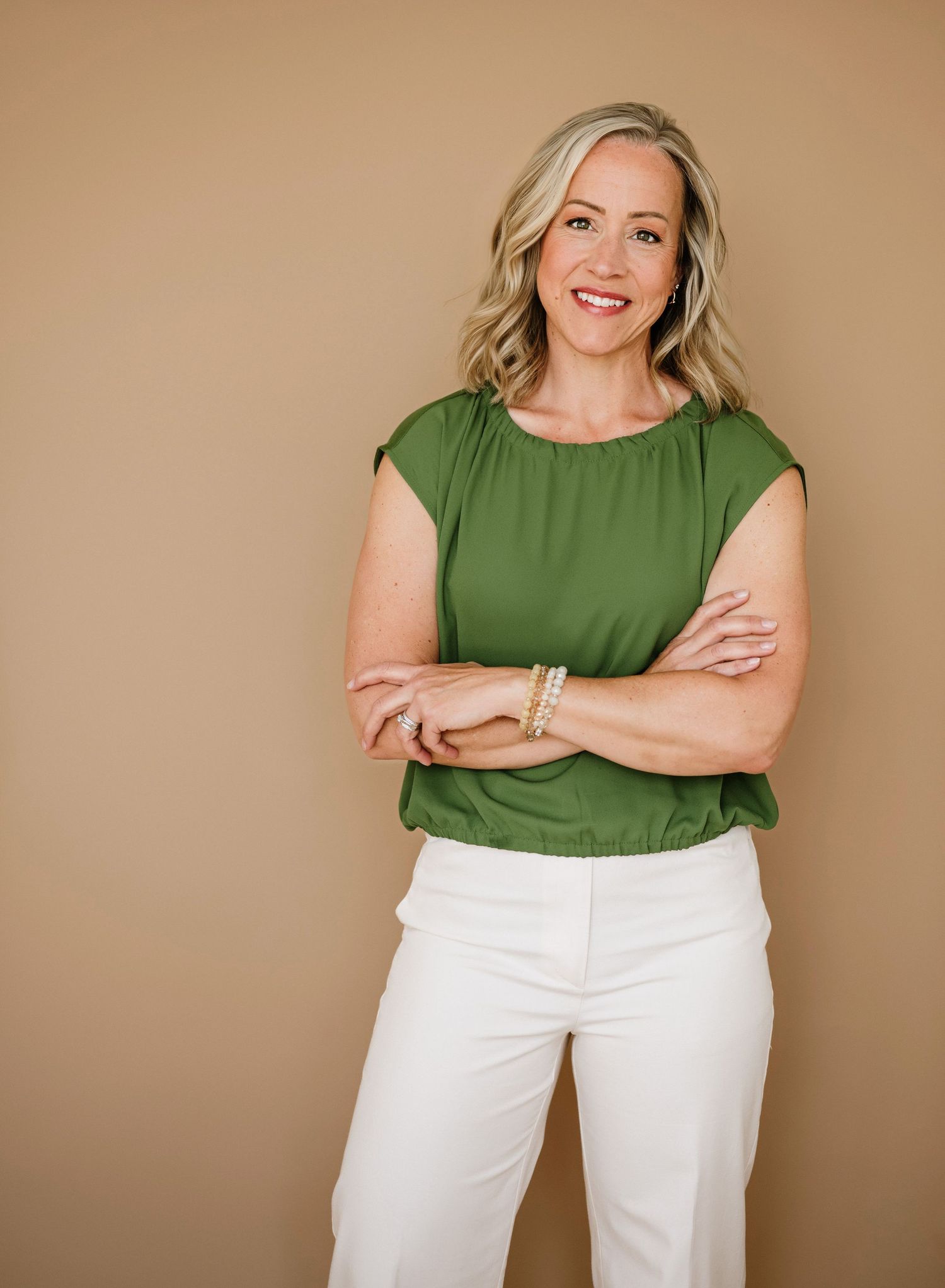 Professional portrait of someone wearing a green cap sleeve blouse and white pants against a neutral brown backdrop.