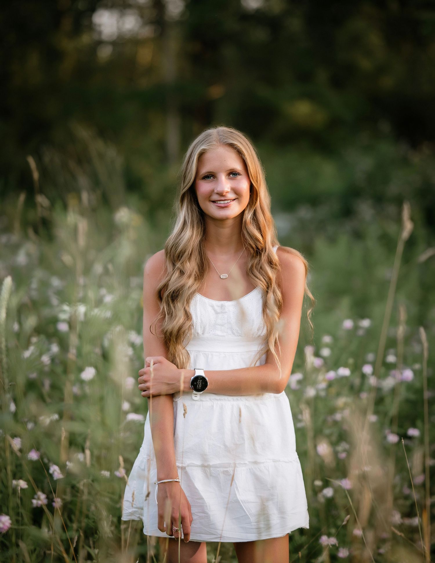 A person in a white summer dress poses in a wildflower meadow at golden hour.
